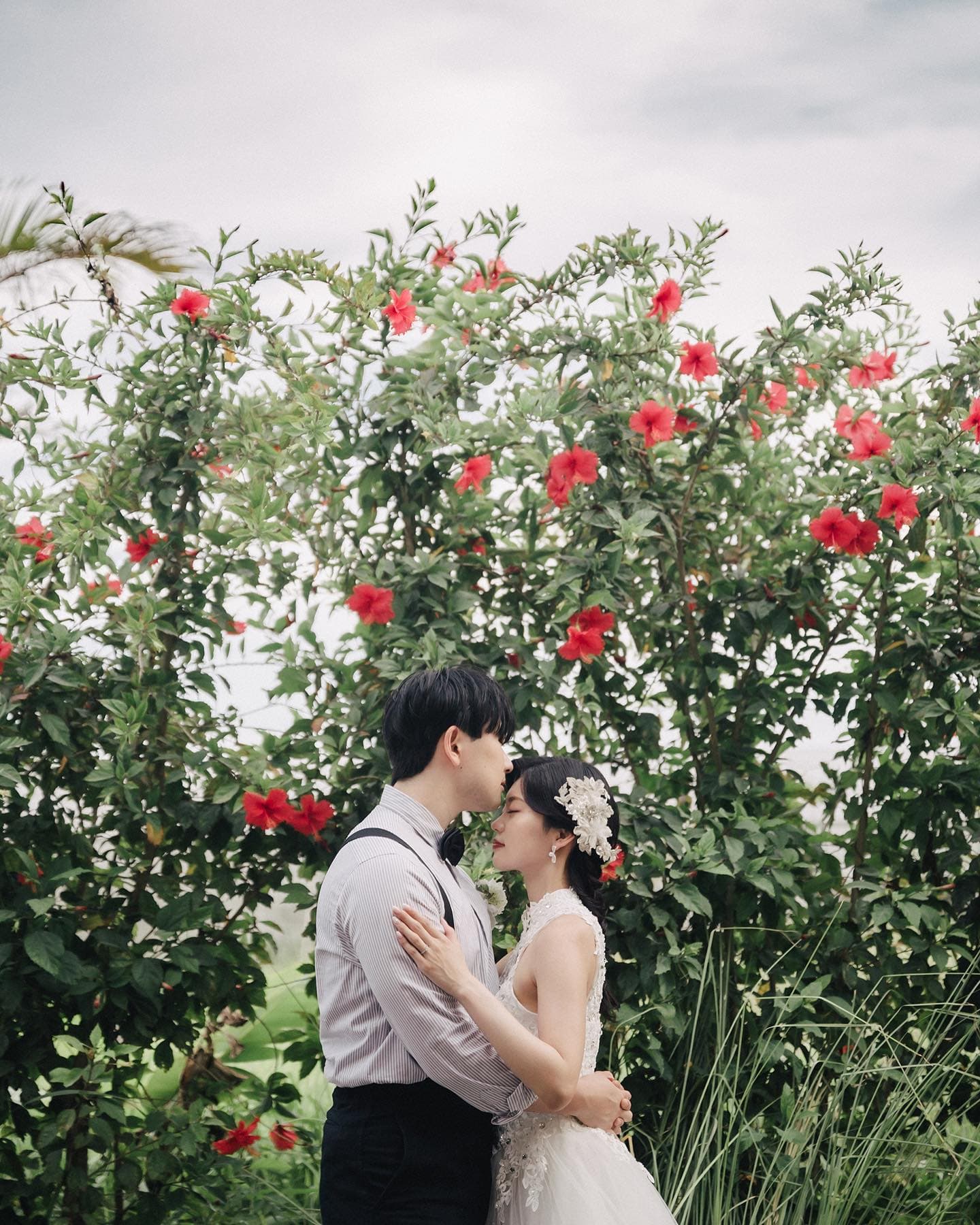Couple touching foreheads before a wall of red hibiscus in Okinawa