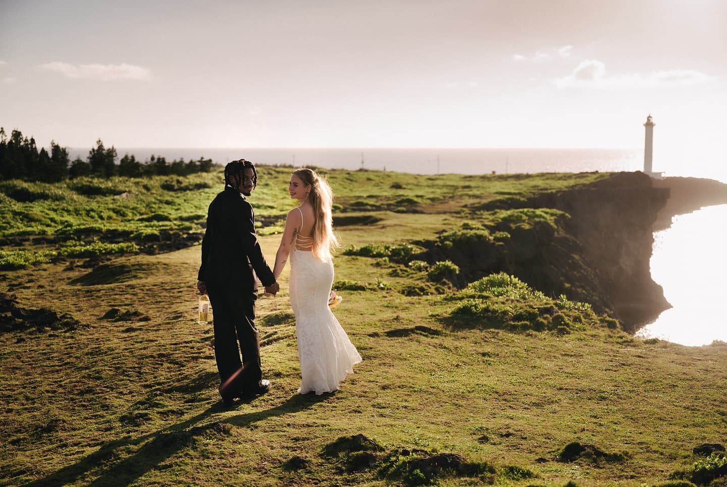 Couple strolling across a green cape toward a lighthouse in soft evening light in Okinawa