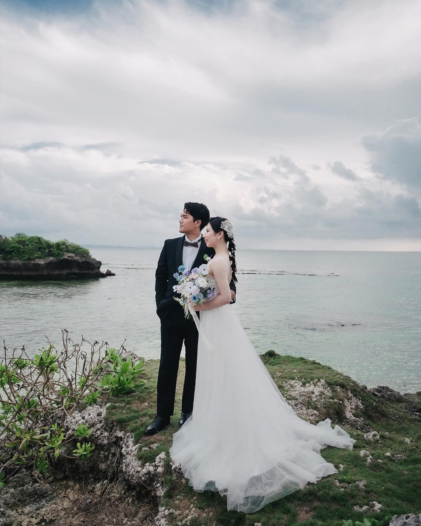 Couple on a grassy cape gazing out to sea under a cloudy Okinawa sky