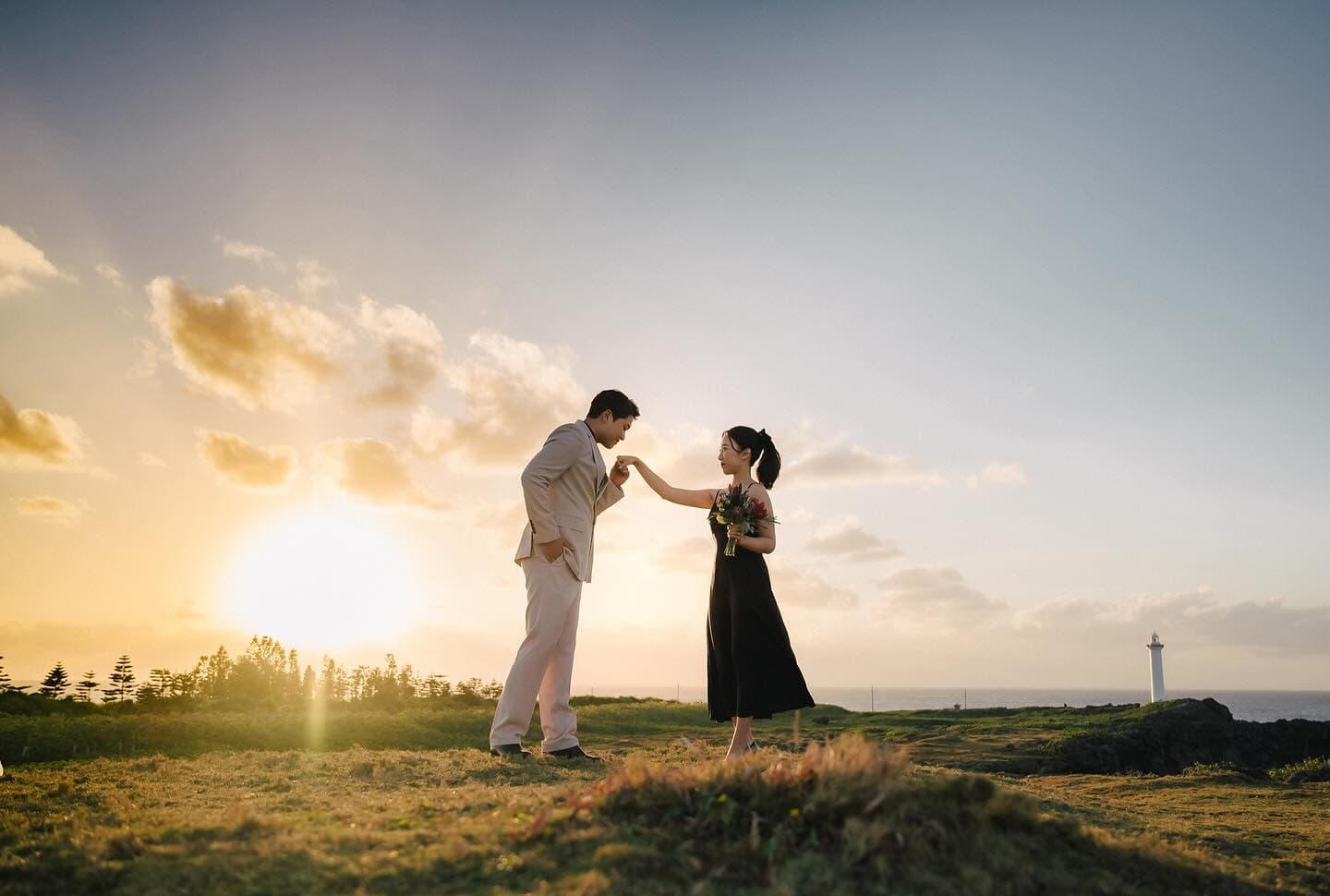 Groom bowing to kiss his bride's hand in a sunset Okinawa meadow