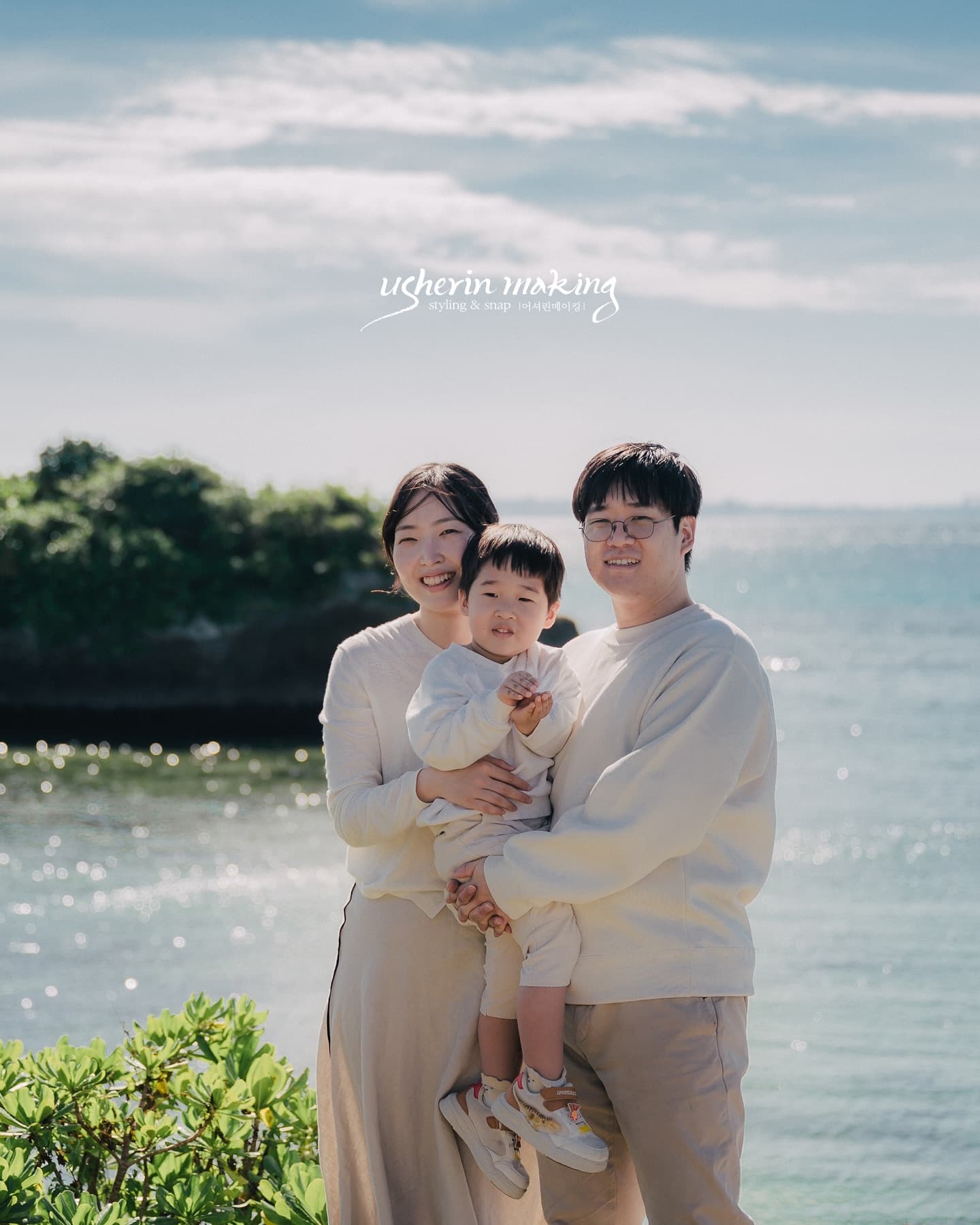 Mother holding their toddler beside the father before a sparkling sea in Okinawa