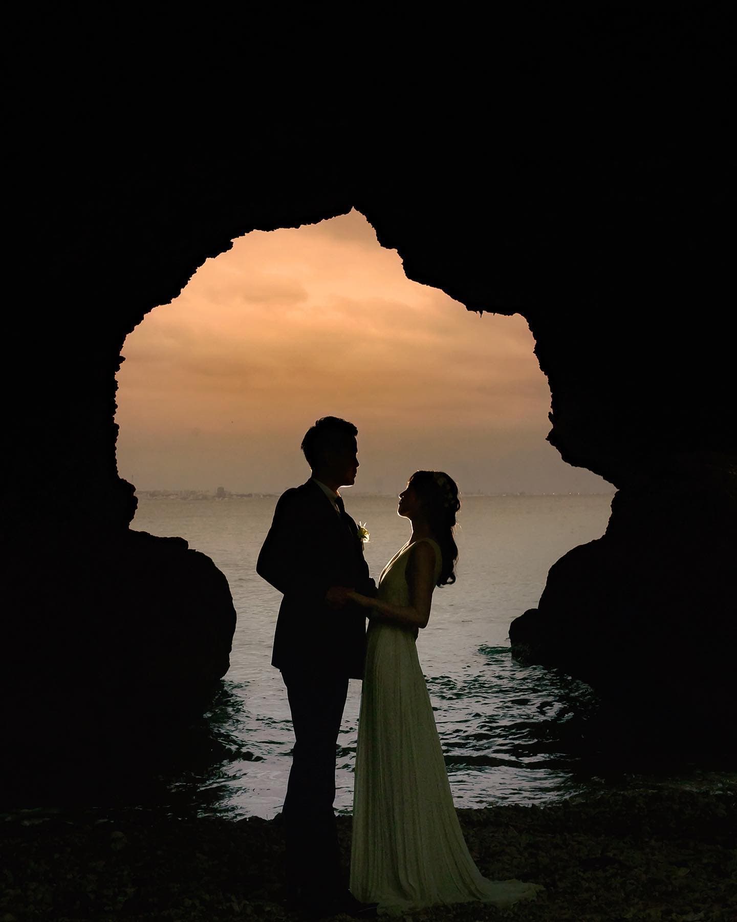 夕焼けの海を望む洞窟で、シルエットになって向かい合う新郎新婦