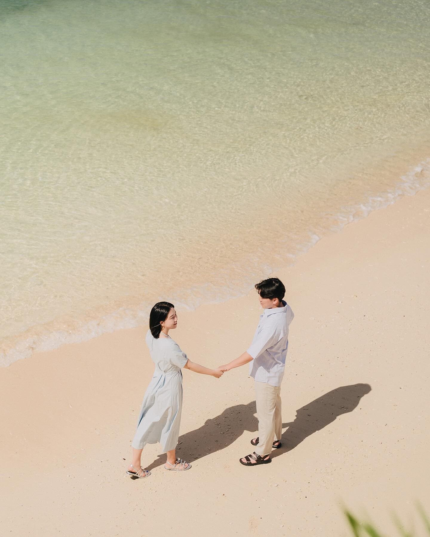 Overhead view of a couple holding hands at the water's edge on a clear Okinawa beach