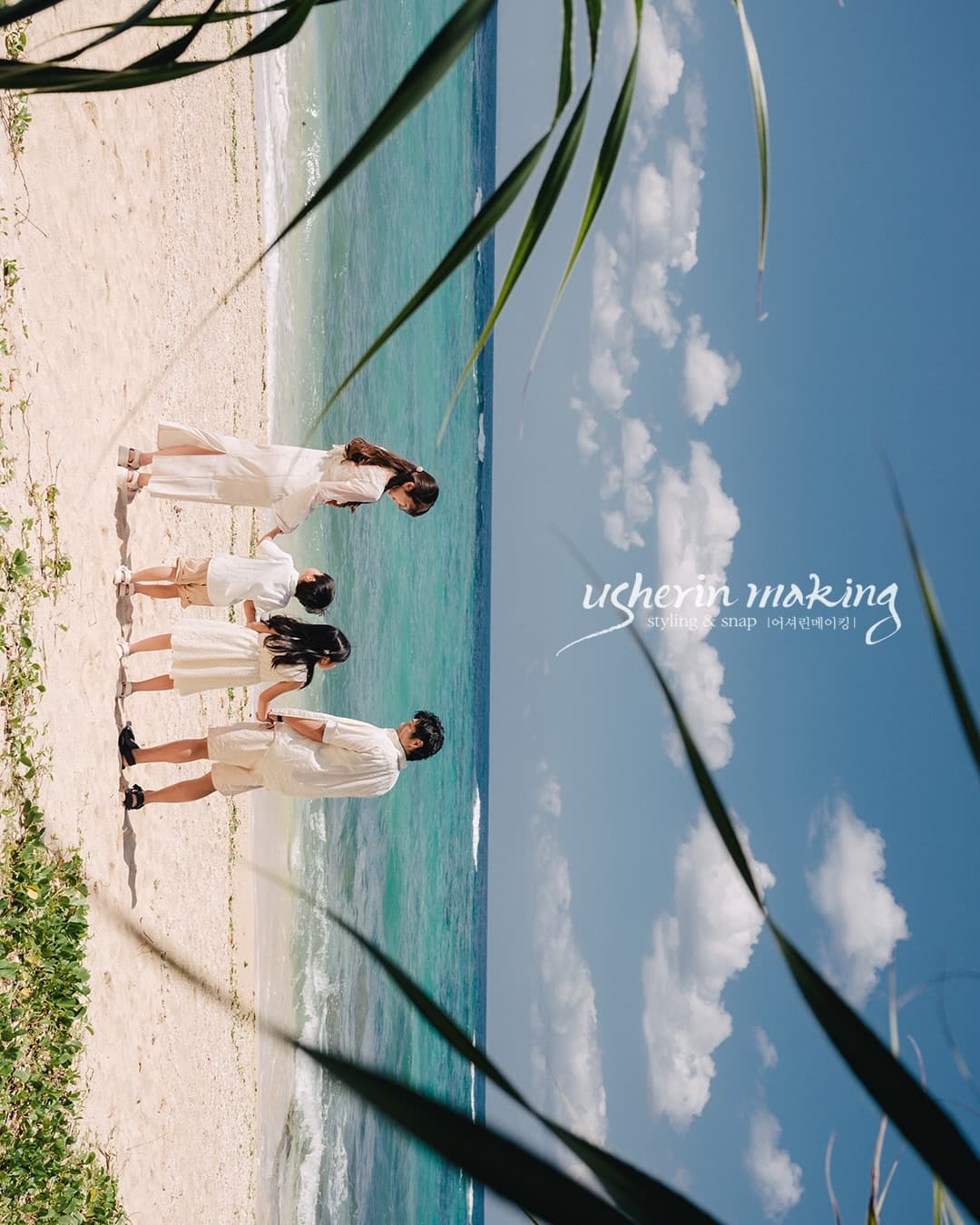 Family in white walking along a white sand beach by the emerald sea in Okinawa