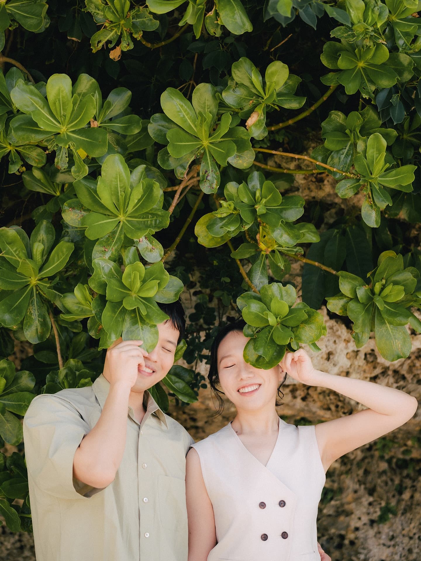 Playful couple hiding behind large green leaves in Okinawa