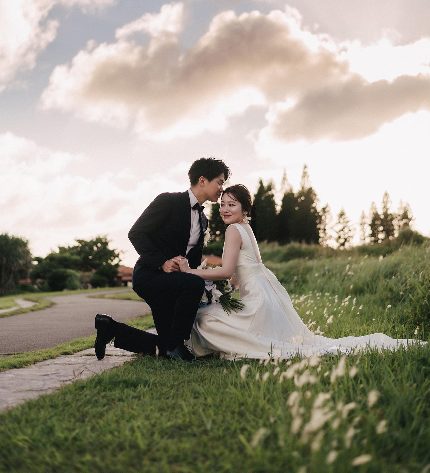 Bride smiling at the camera as the groom leans close in a grassy field