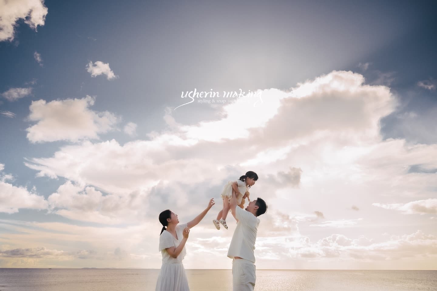 Father lifting the baby high under a wide blue sky at an Okinawa beach as mom reaches up