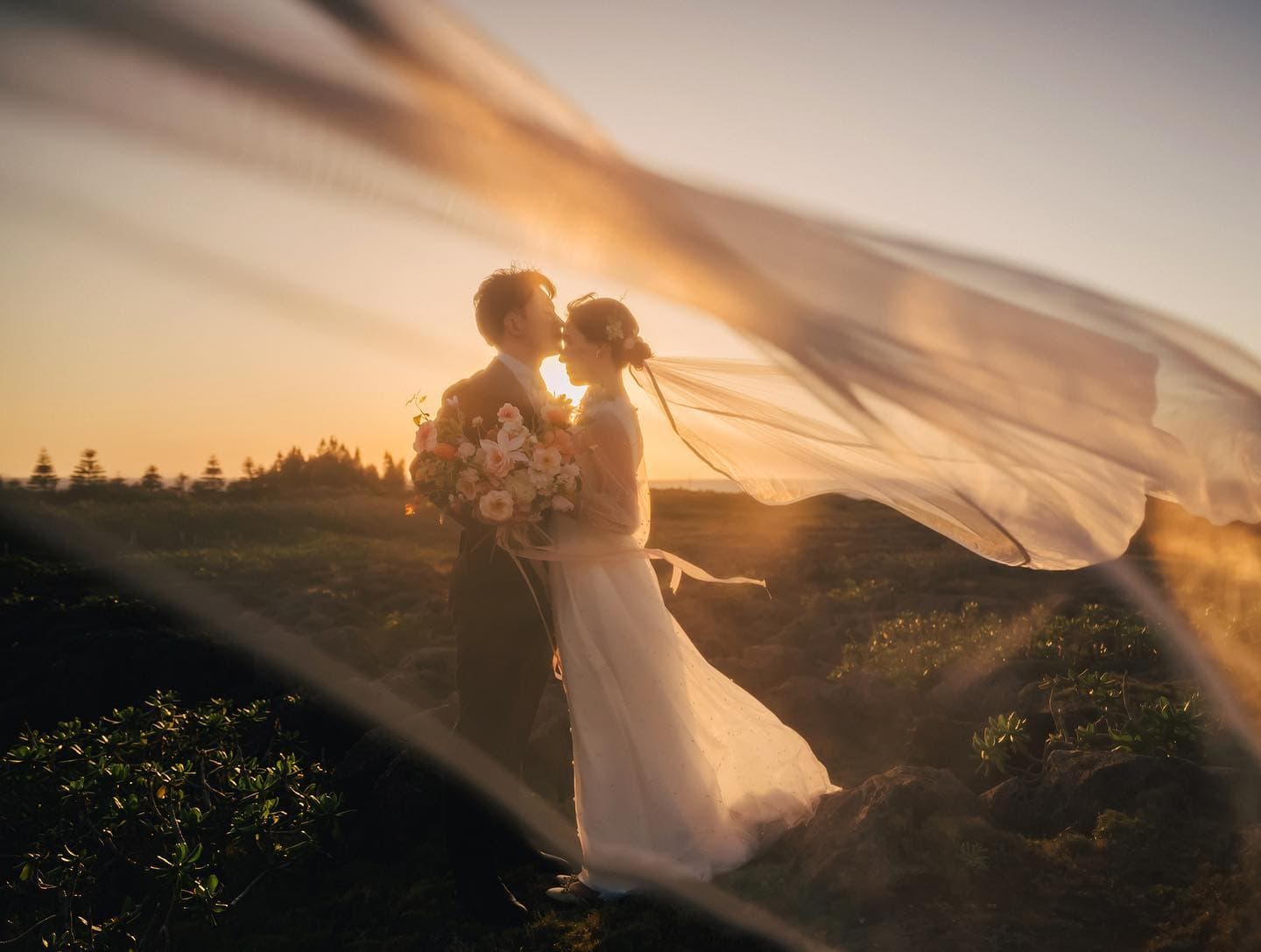 Couple kissing in golden sunset light seen through a sweeping veil in Okinawa