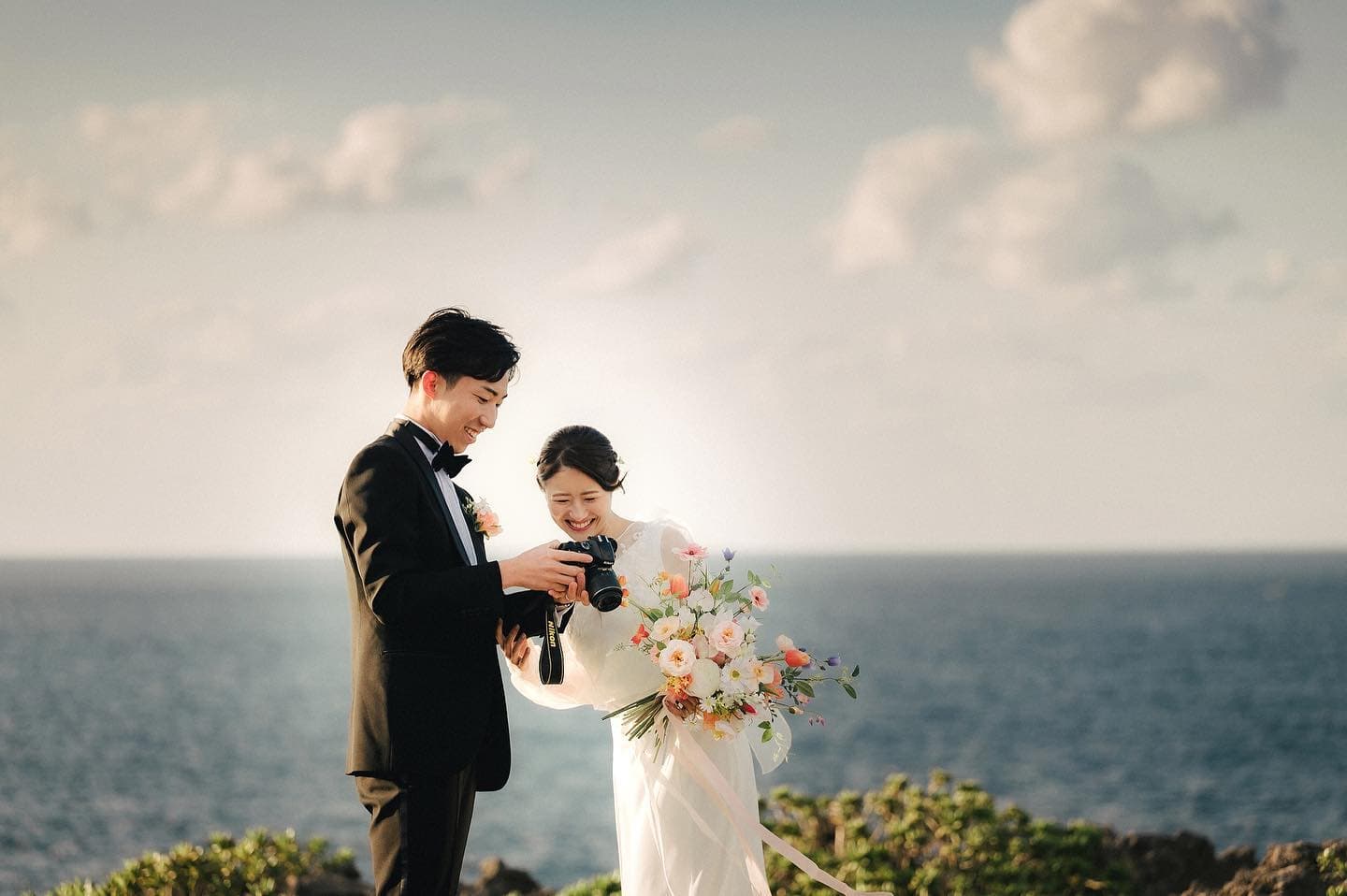 海を背にカメラの写真を新婦に見せる新郎