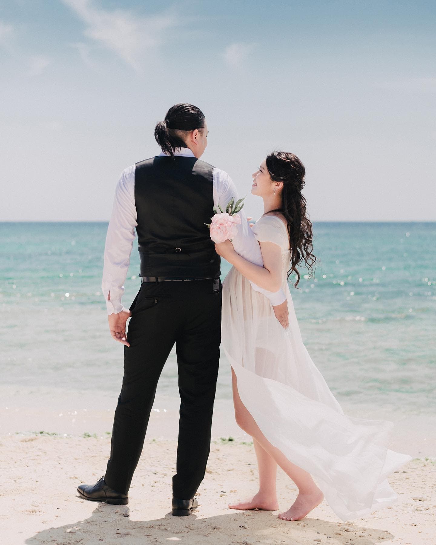 Seen from behind, an expectant couple embrace by the turquoise Okinawa sea