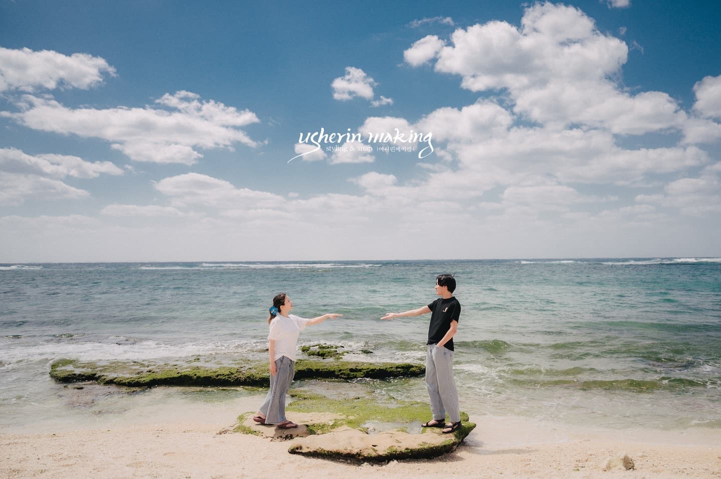 On a seaside rock, a couple reach out their hands under Okinawa's blue sky