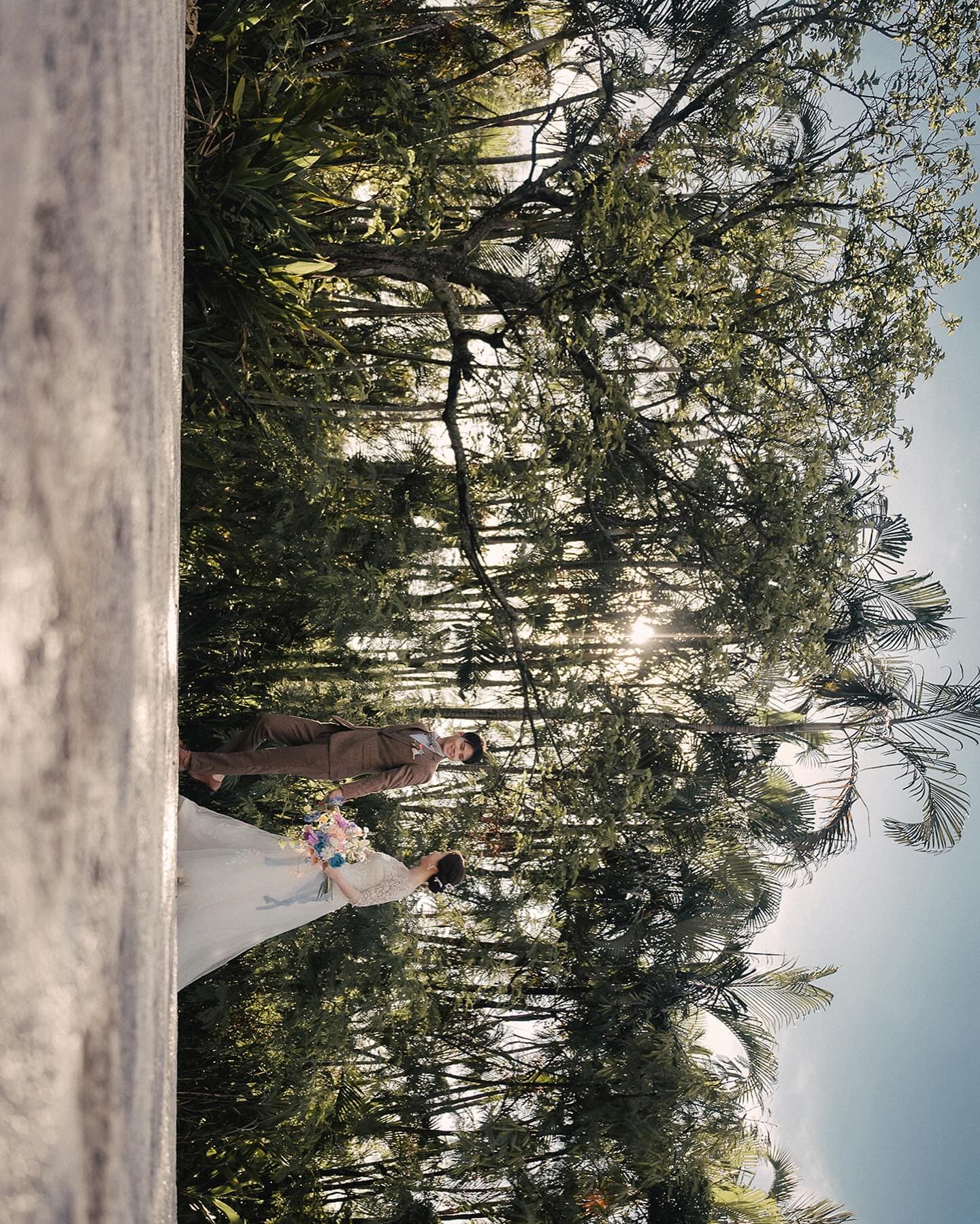 Bride and groom strolling through a sunlit grove in Okinawa with a colorful bouquet