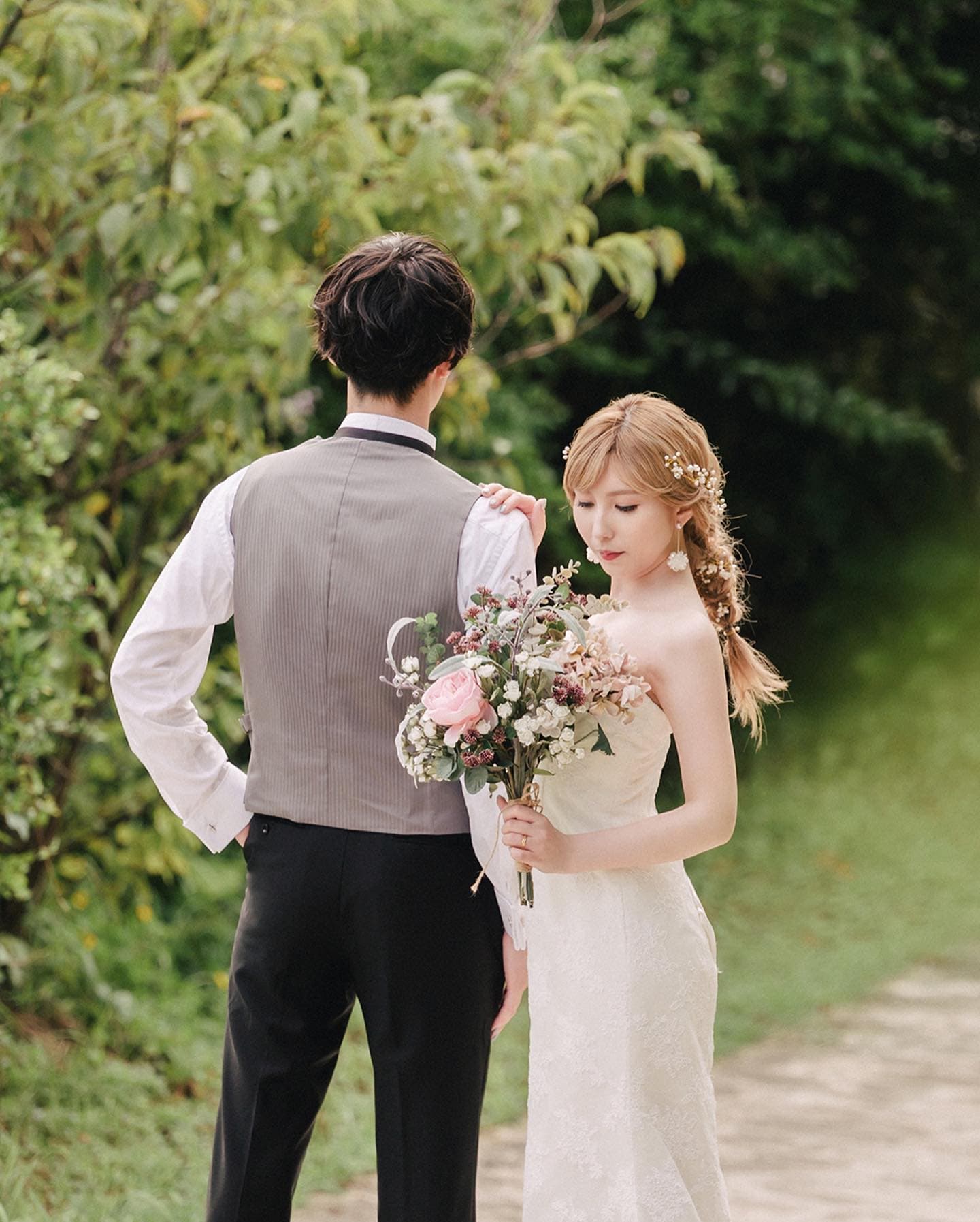 Bride resting a hand on the groom's shoulder along a leafy path in Okinawa
