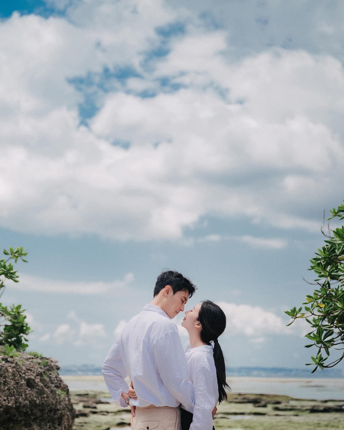 A couple in white shirts gazes at each other under towering summer clouds, Okinawa