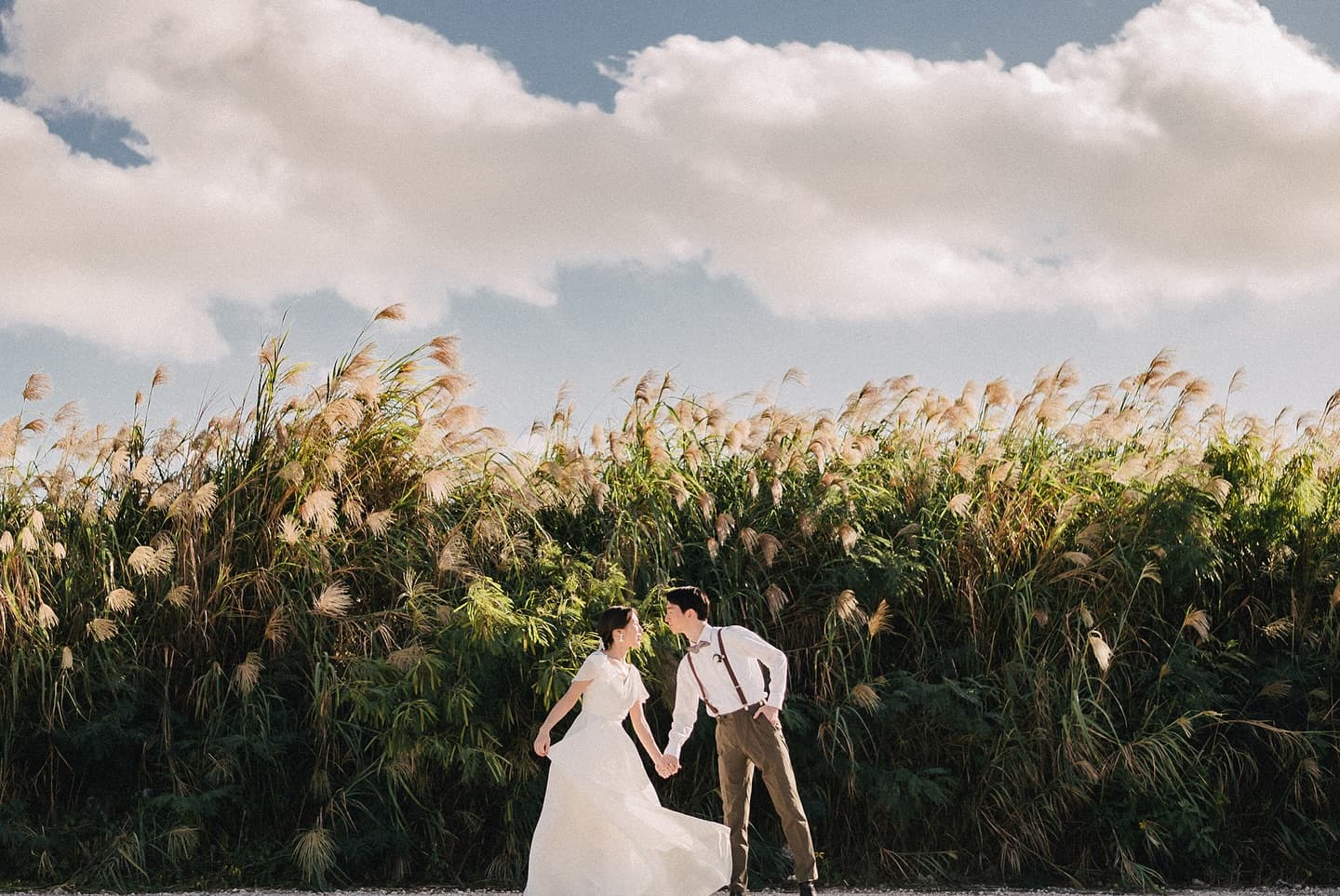 Bride and groom leaning in for a kiss by swaying pampas grass in Okinawa