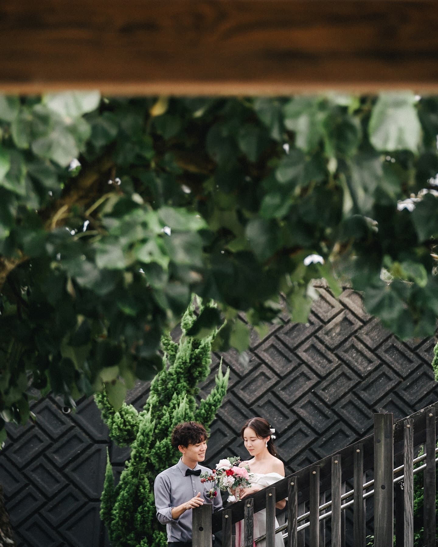 Bride and groom on a wooden deck under lush greenery in Okinawa