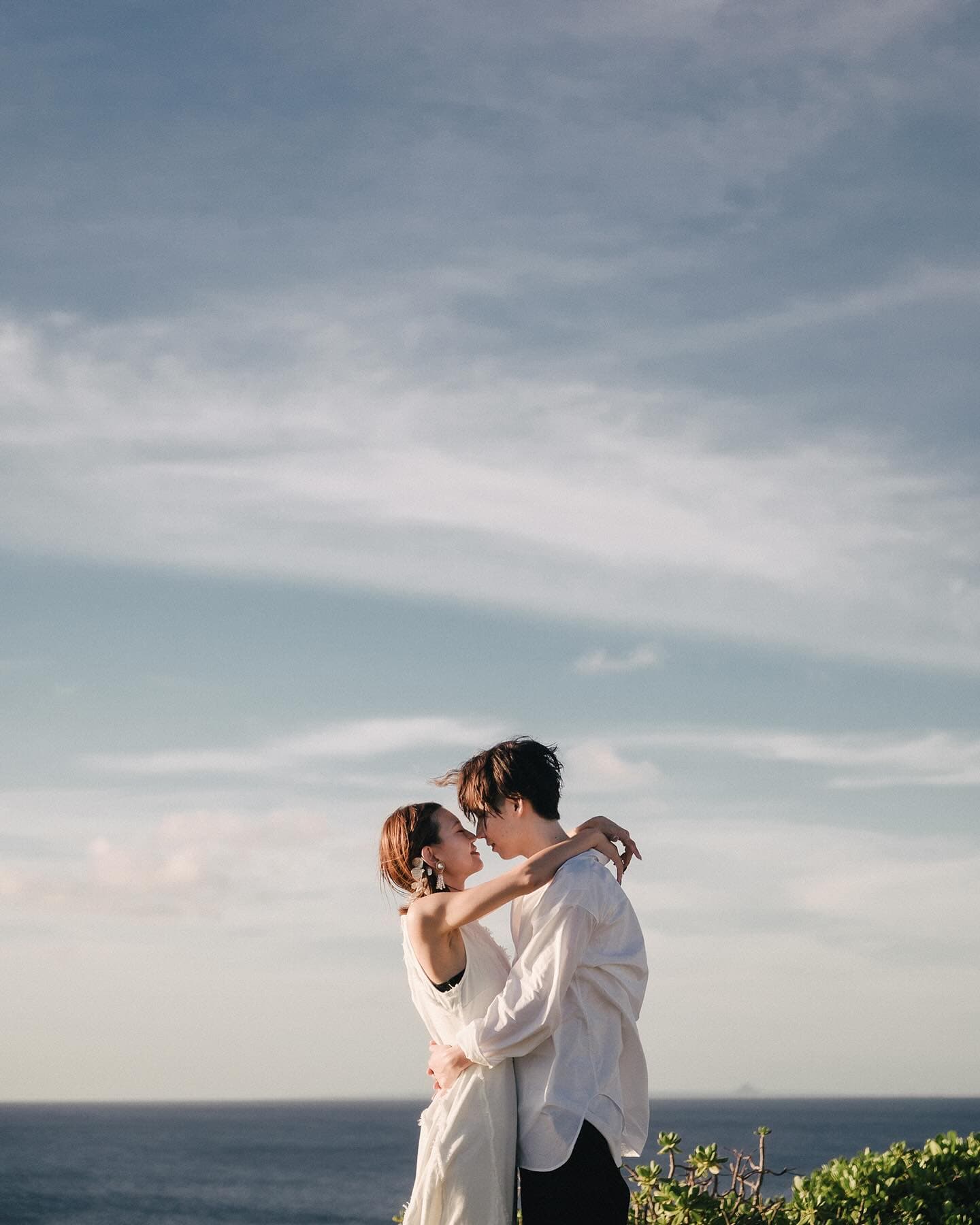 Couple embracing on a seaside bluff under a wide Okinawa sky