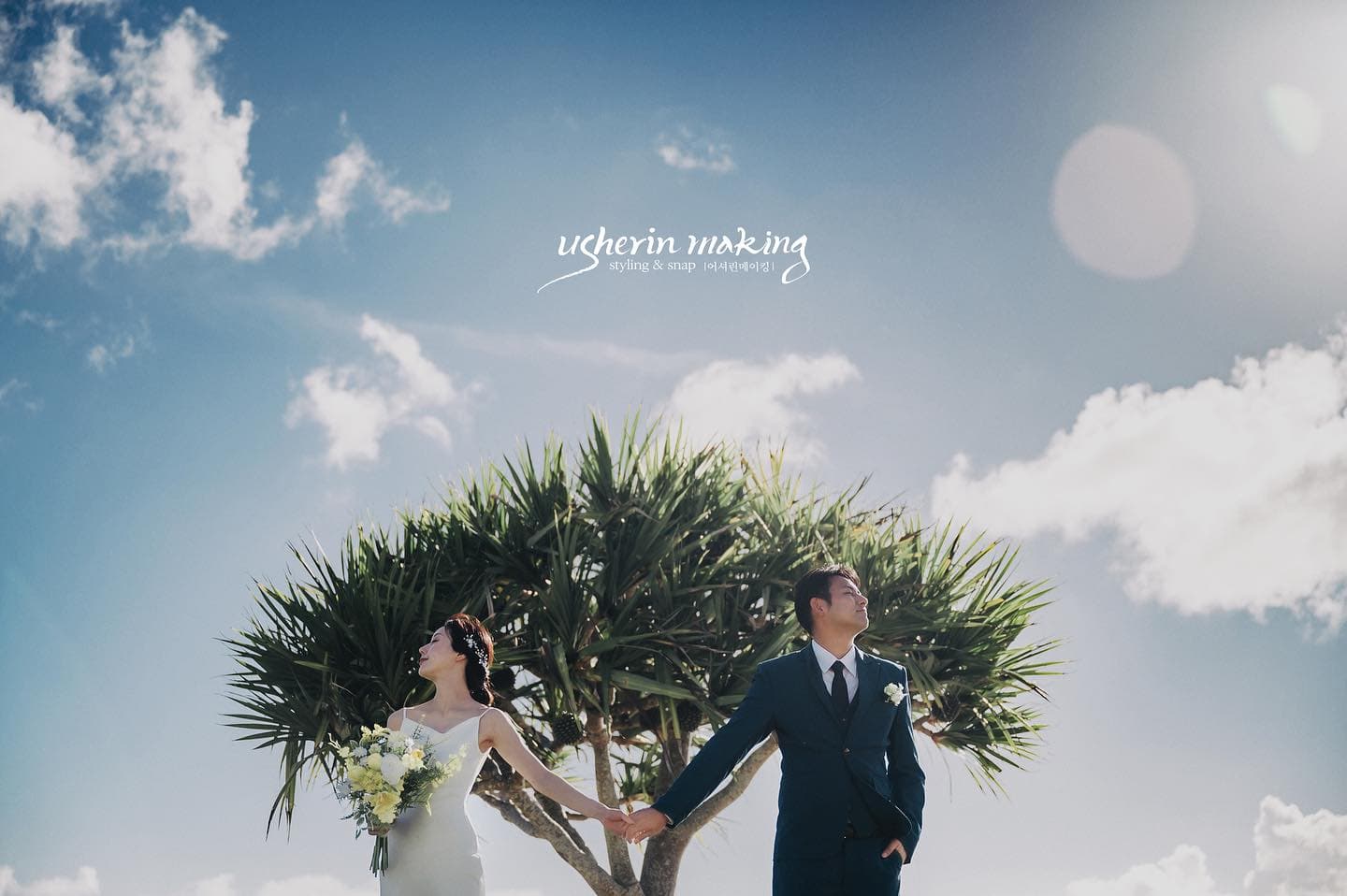 Couple hold hands beneath a pandanus tree under a bright Okinawa sky
