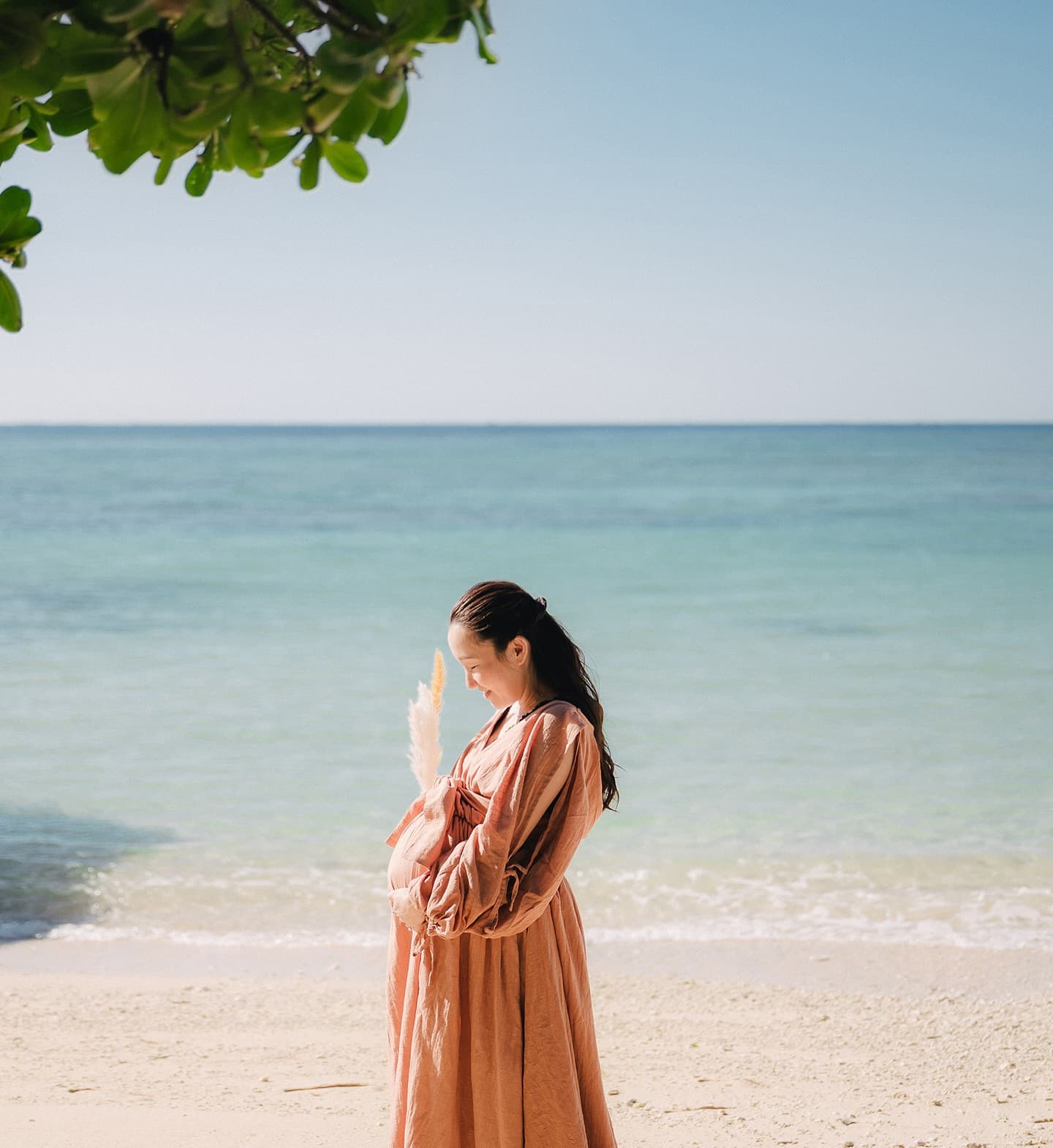 Expectant mother in a terracotta dress on a sunny Okinawa beach