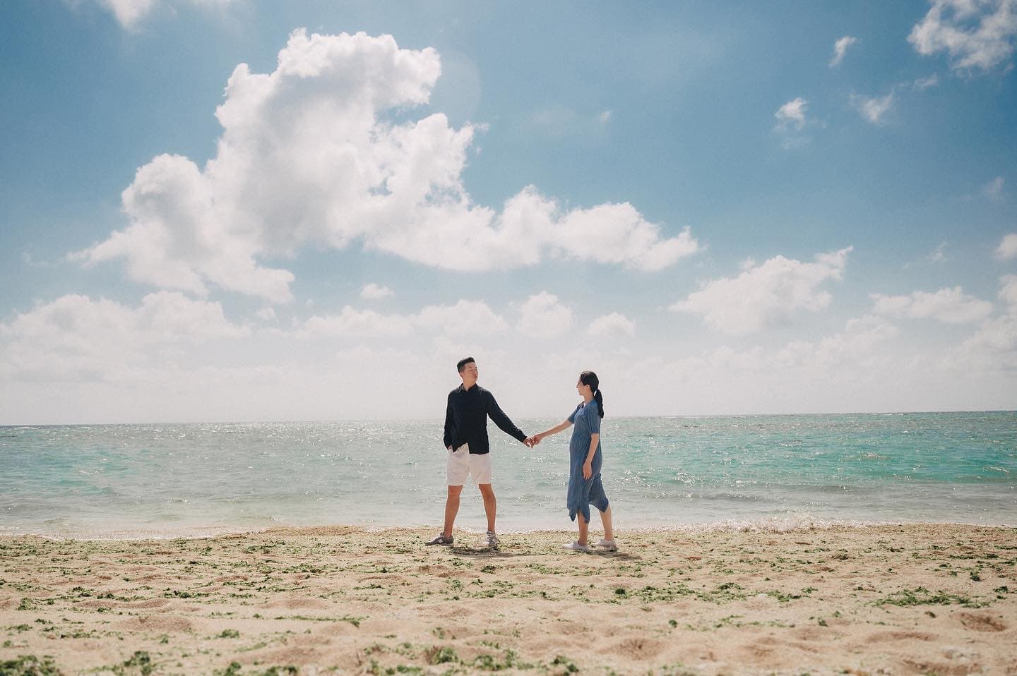 エメラルドの海辺で手を取り合う妊婦と夫