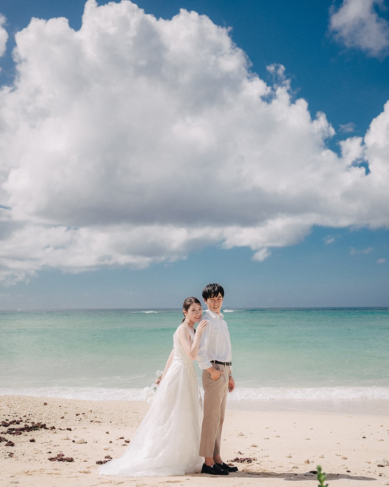 Bride and groom on a white Okinawa beach beneath a towering cloud