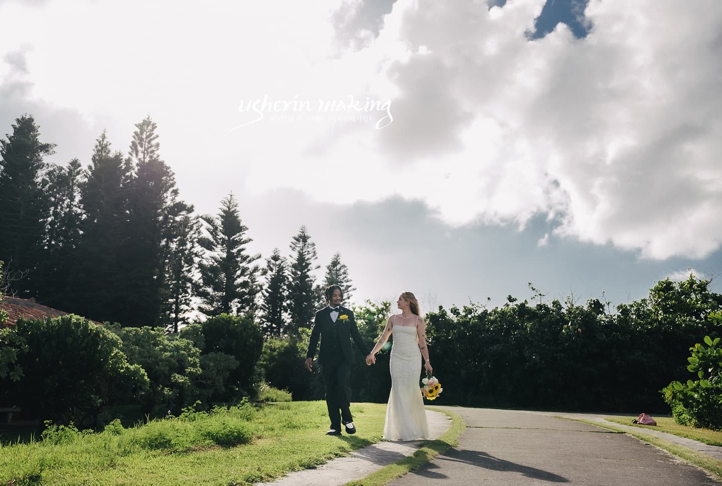 Bride and groom walking hand in hand along a tree-lined path on a sunny day in Okinawa