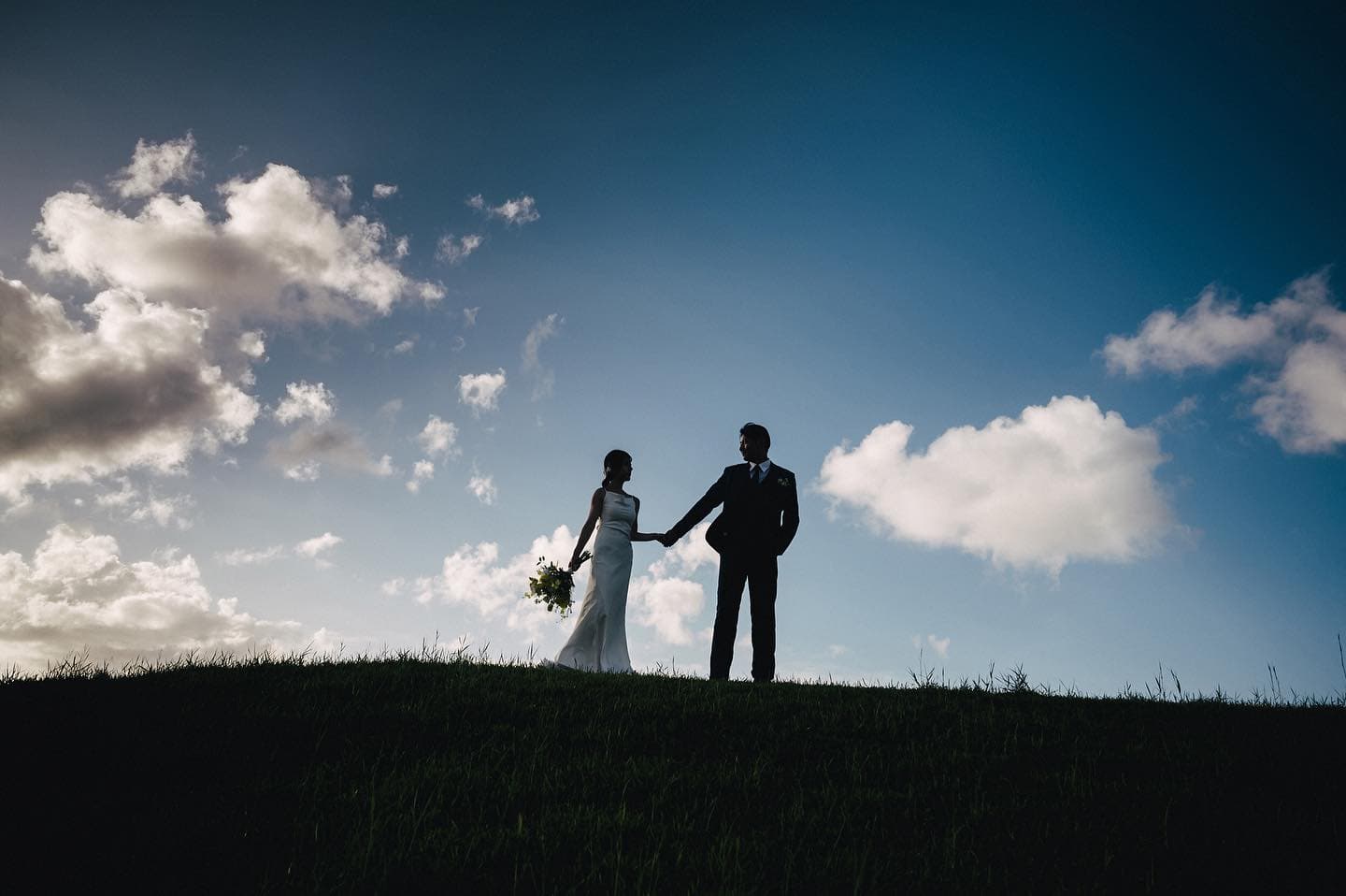 Silhouetted couple hold hands on a grassy ridge in Okinawa