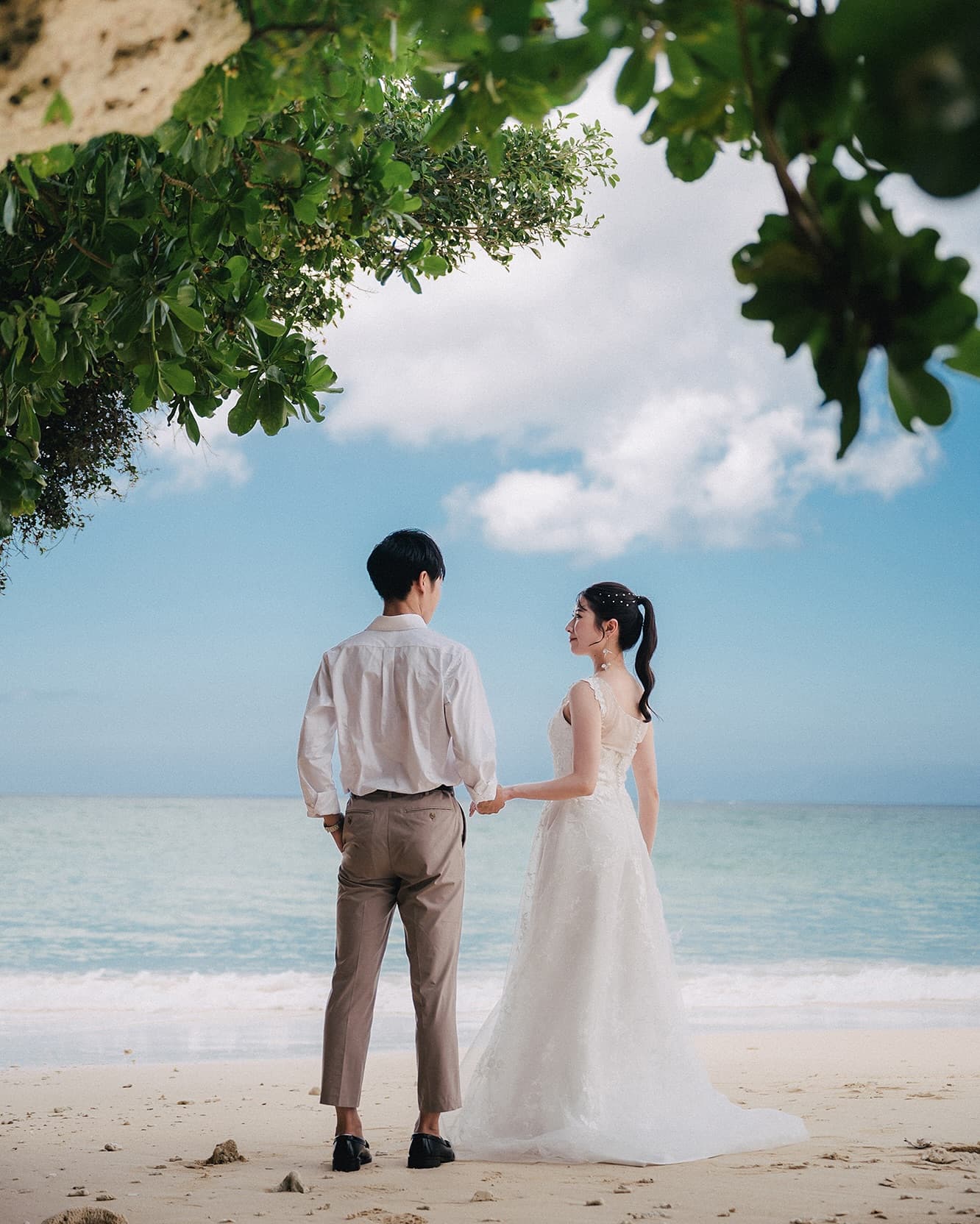 Couple holding hands facing the Okinawa sea, seen from behind