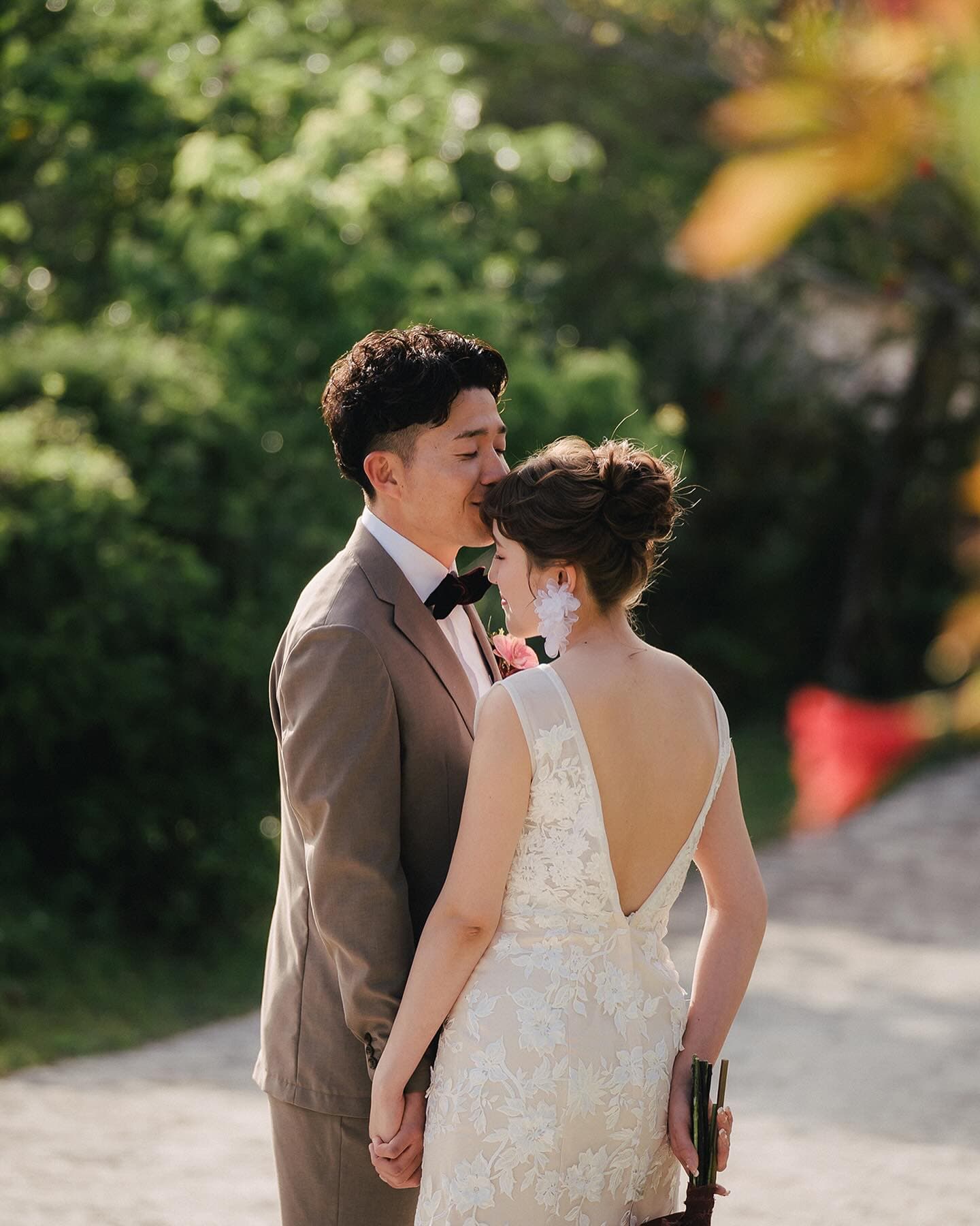 Groom kisses the bride's forehead on a sunlit Okinawa path