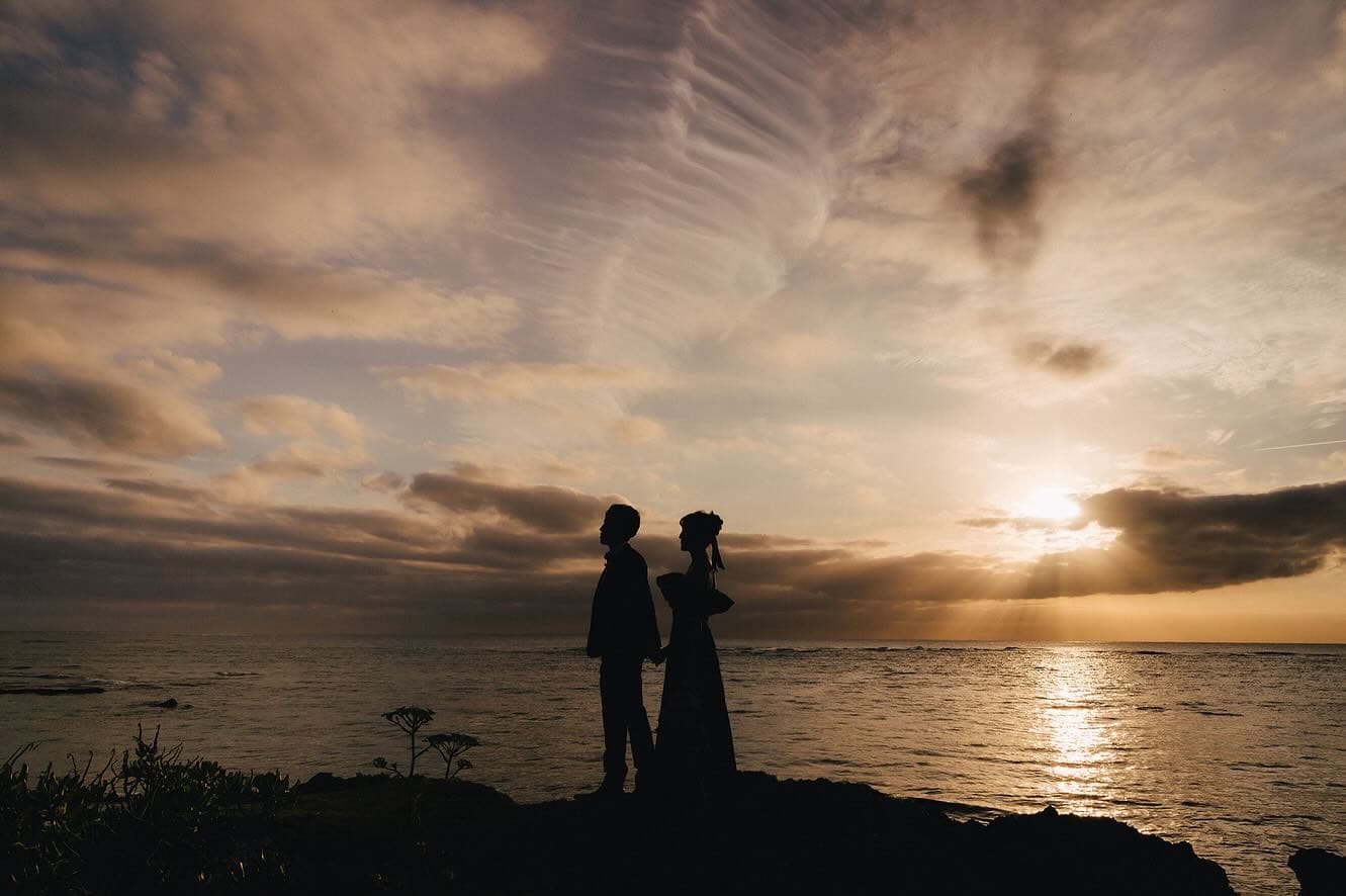 Silhouetted bride and groom on coastal rocks at a glowing Okinawa sunset
