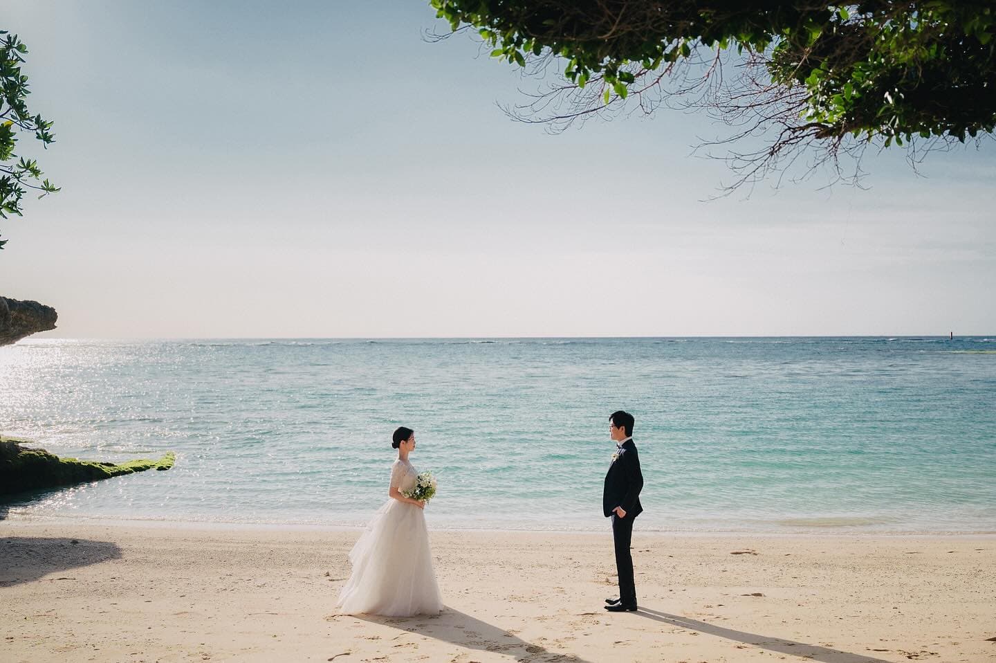 Bride and groom face each other across a white sand Okinawa beach