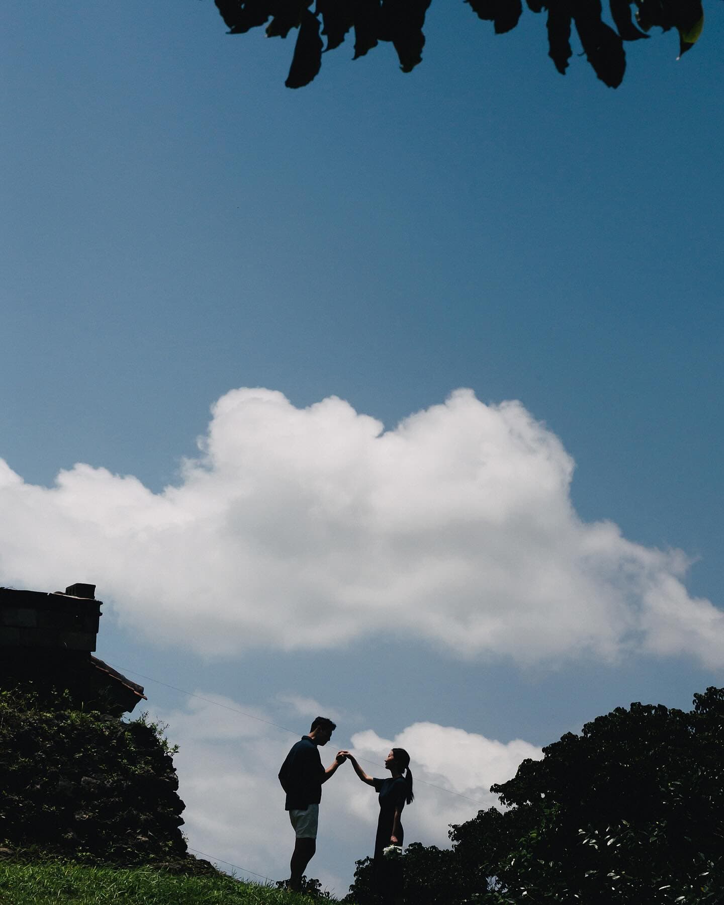 Silhouette of a couple joining hands against blue sky and clouds in Okinawa