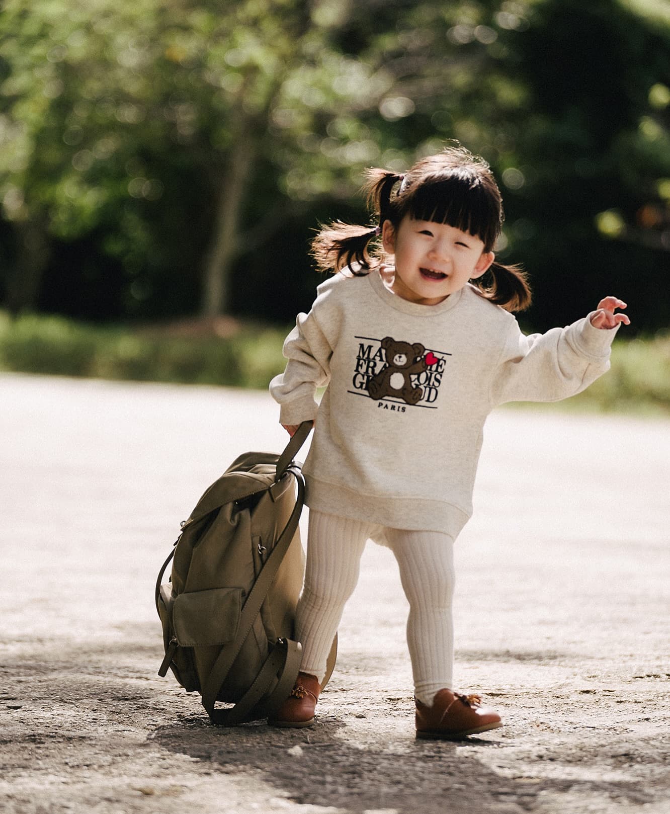 リュックを引いて笑うおさげ髪の女の子、晴れた沖縄の道で