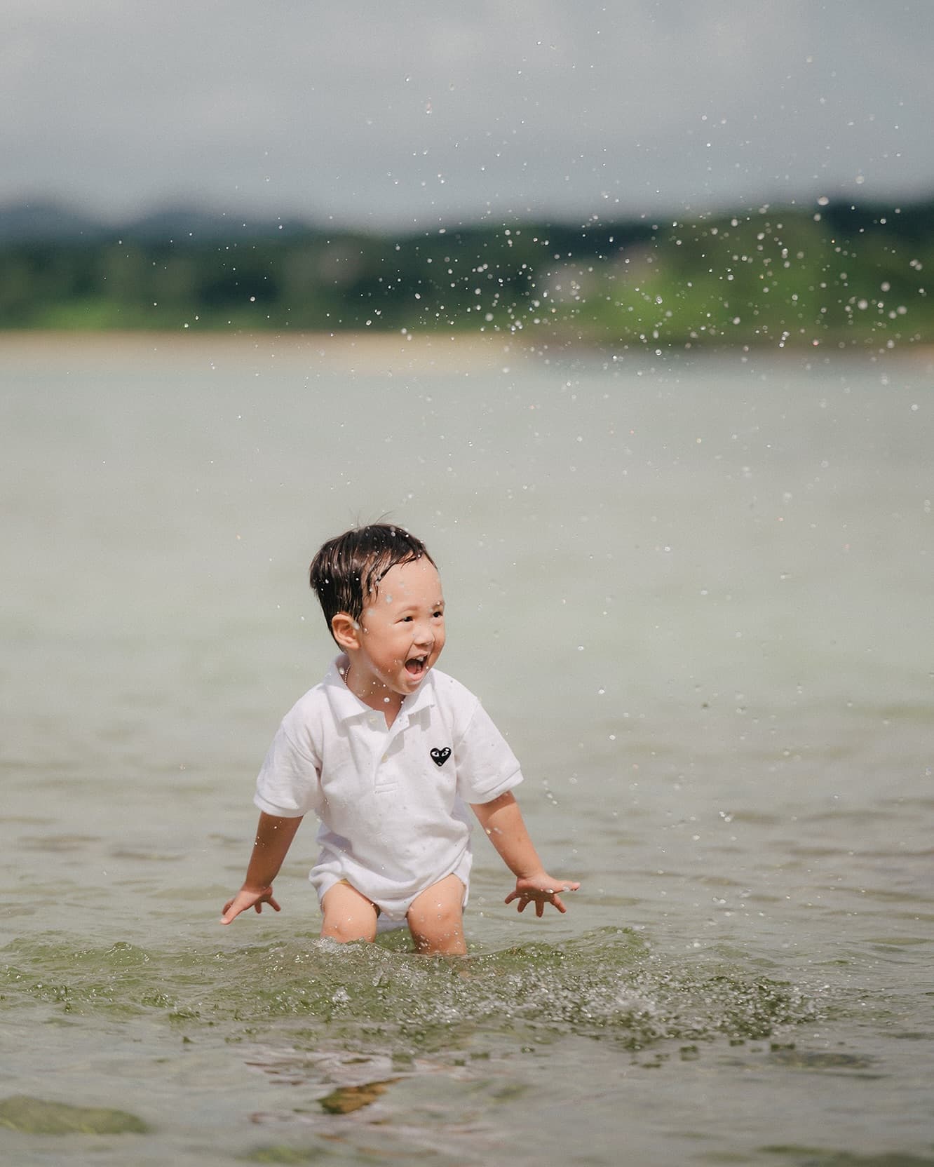 曇り空の沖縄の海、浅瀬で水しぶきを上げて大はしゃぎする幼い子ども