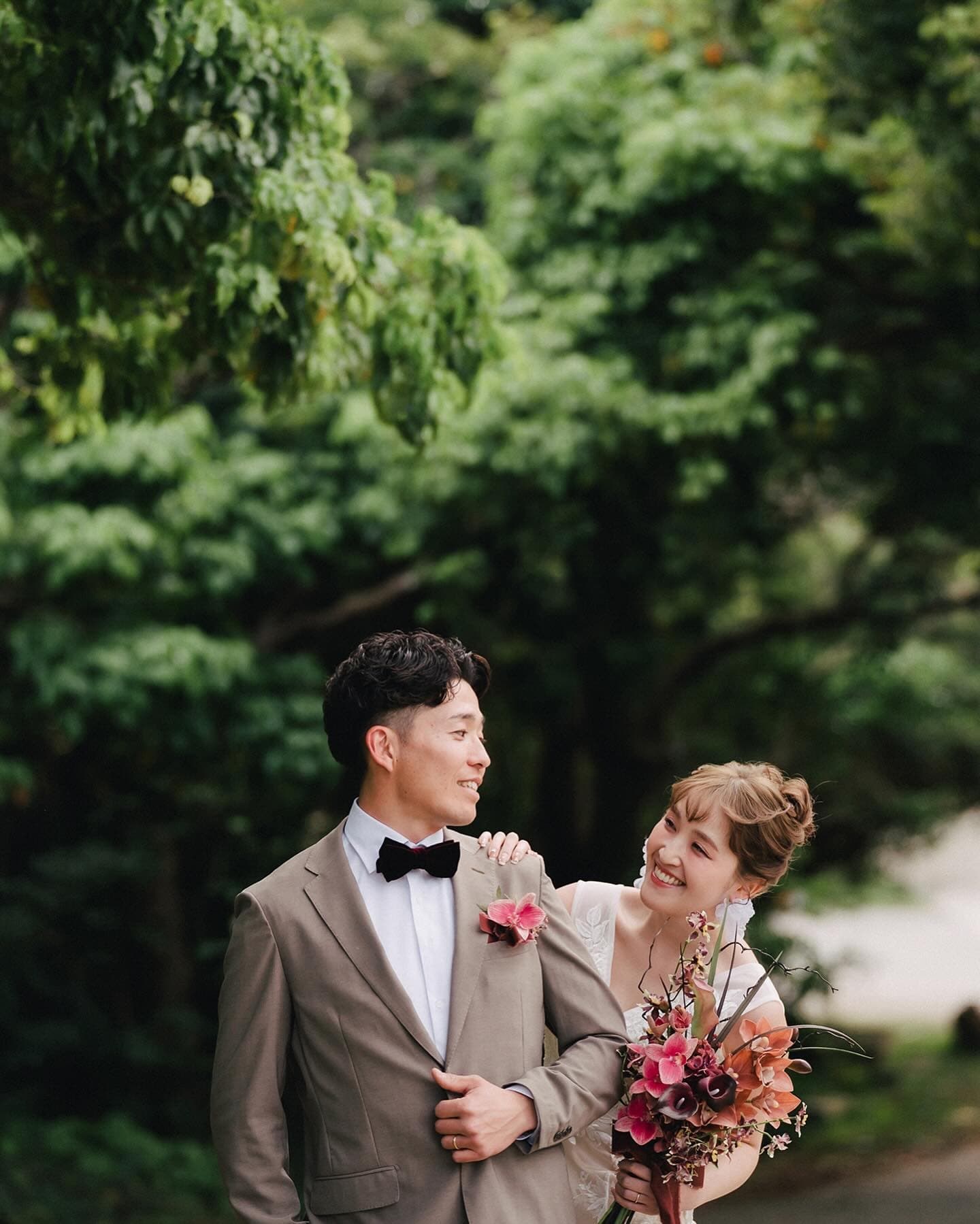 Bride and groom share a laugh under green trees in Okinawa
