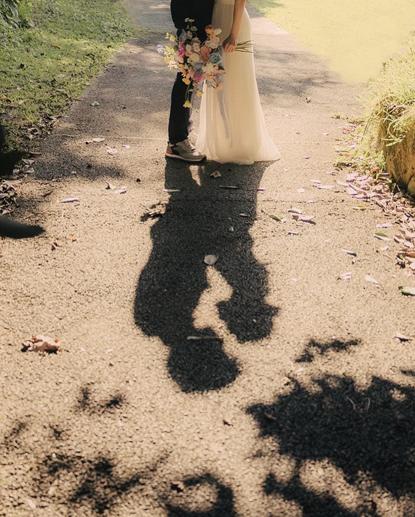 The couple's shadows stretching across a path, with bouquet and dress hem in view