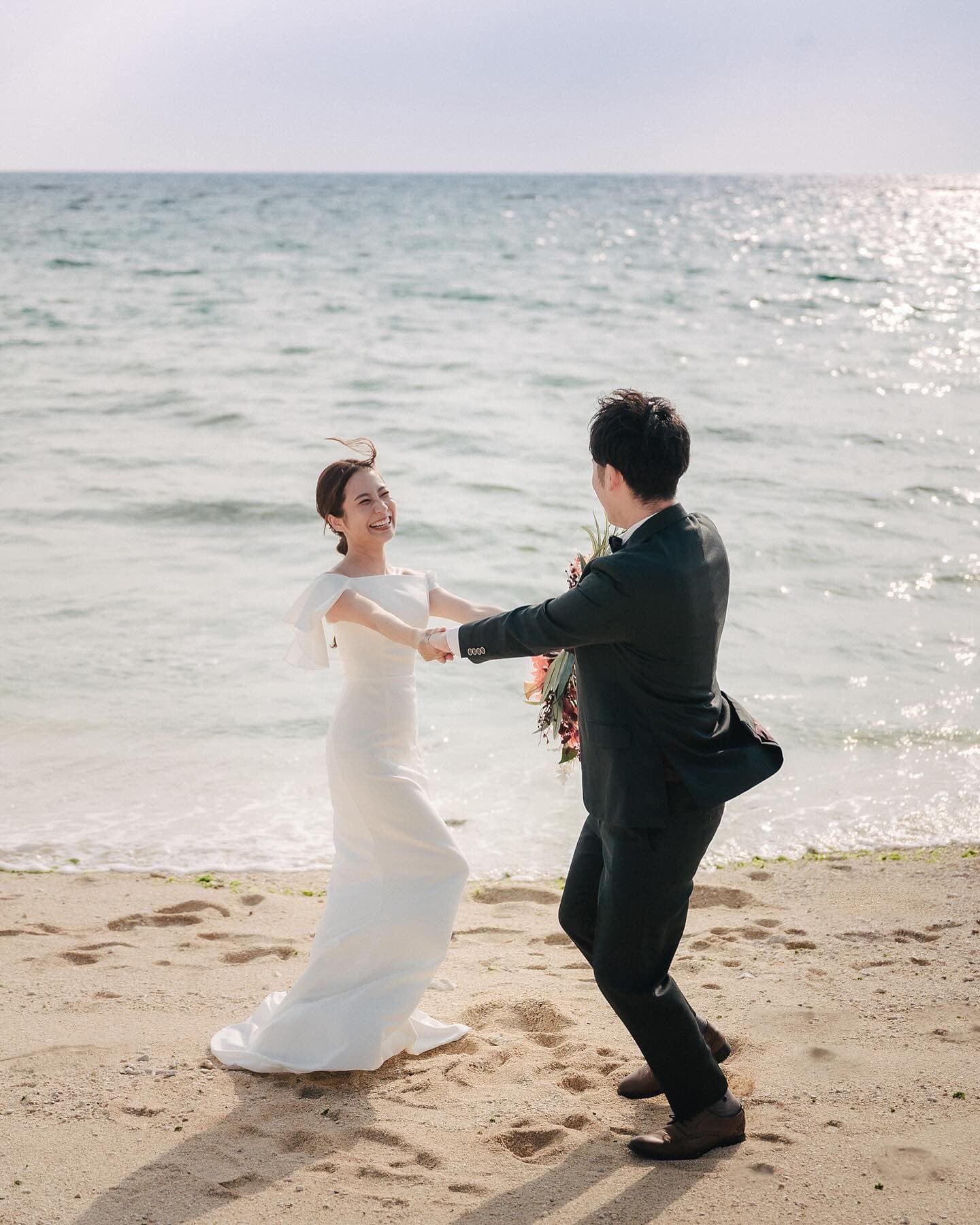 Bride and groom playfully dancing hand in hand on a sandy Okinawa beach