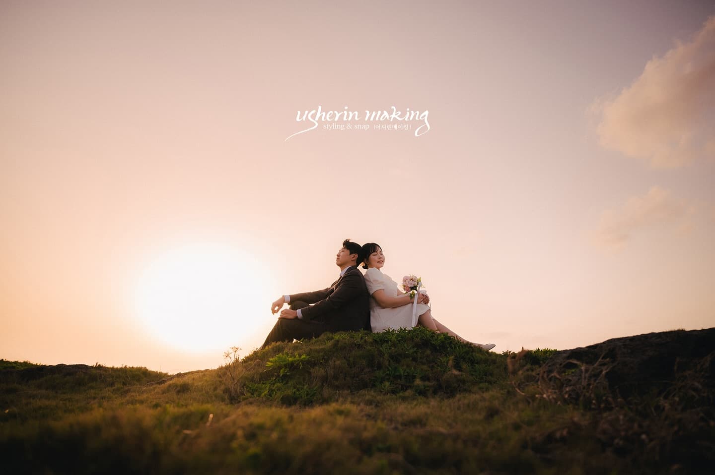 Couple sitting back to back on a grassy hill at sunset in Okinawa