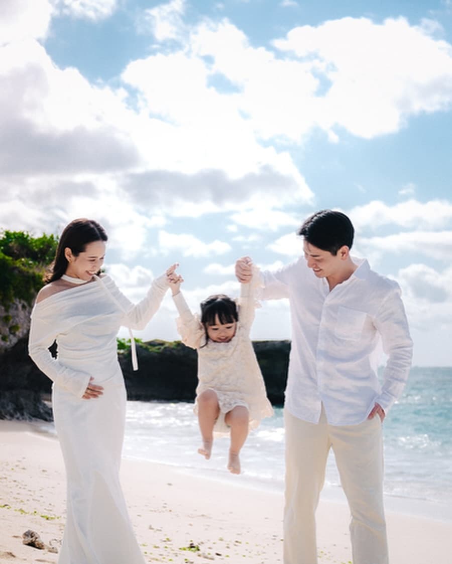 Parents swinging their little daughter by the hands on a bright Okinawa beach