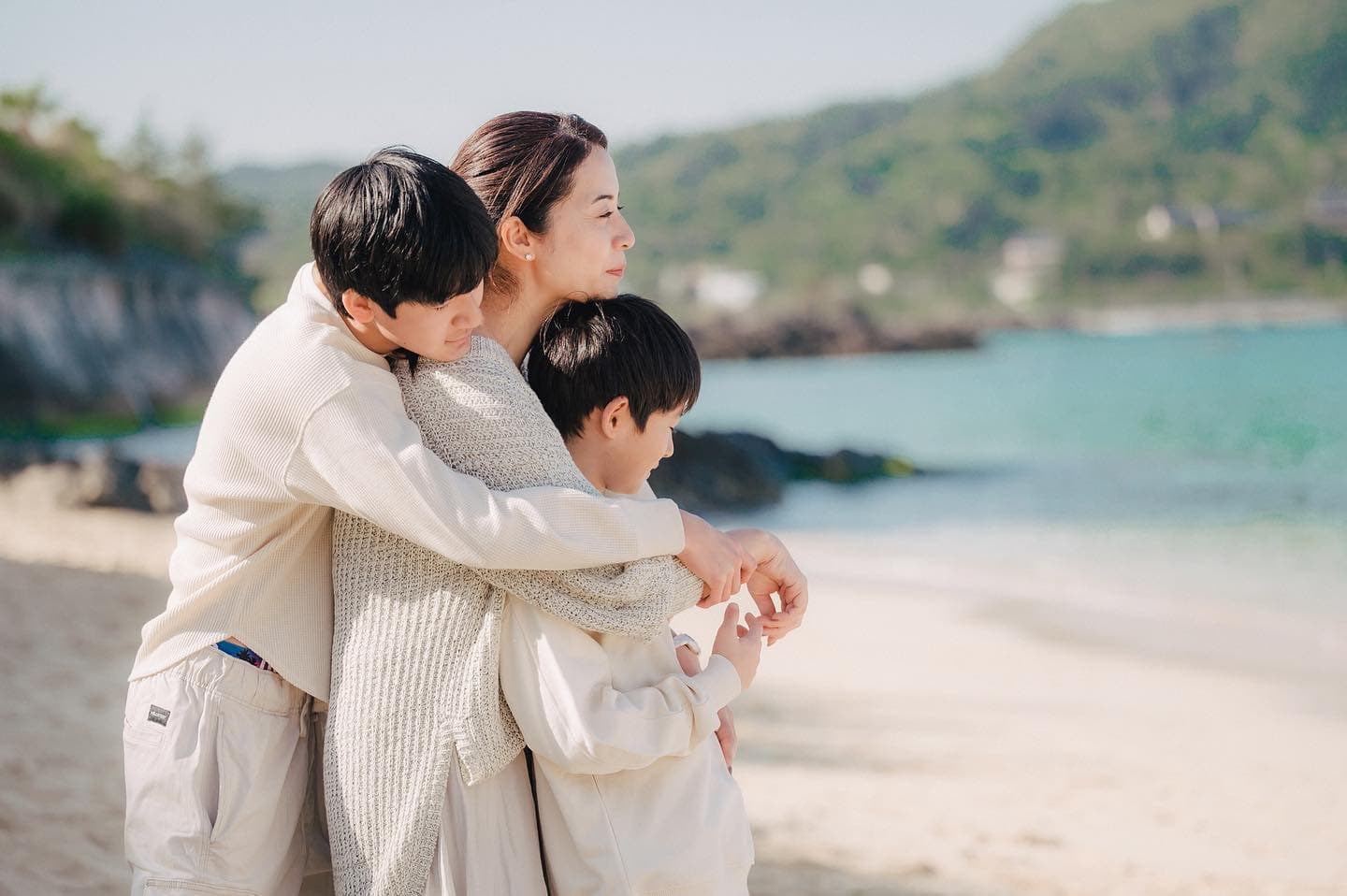 沖縄の海辺で二人の息子を抱きしめる母親