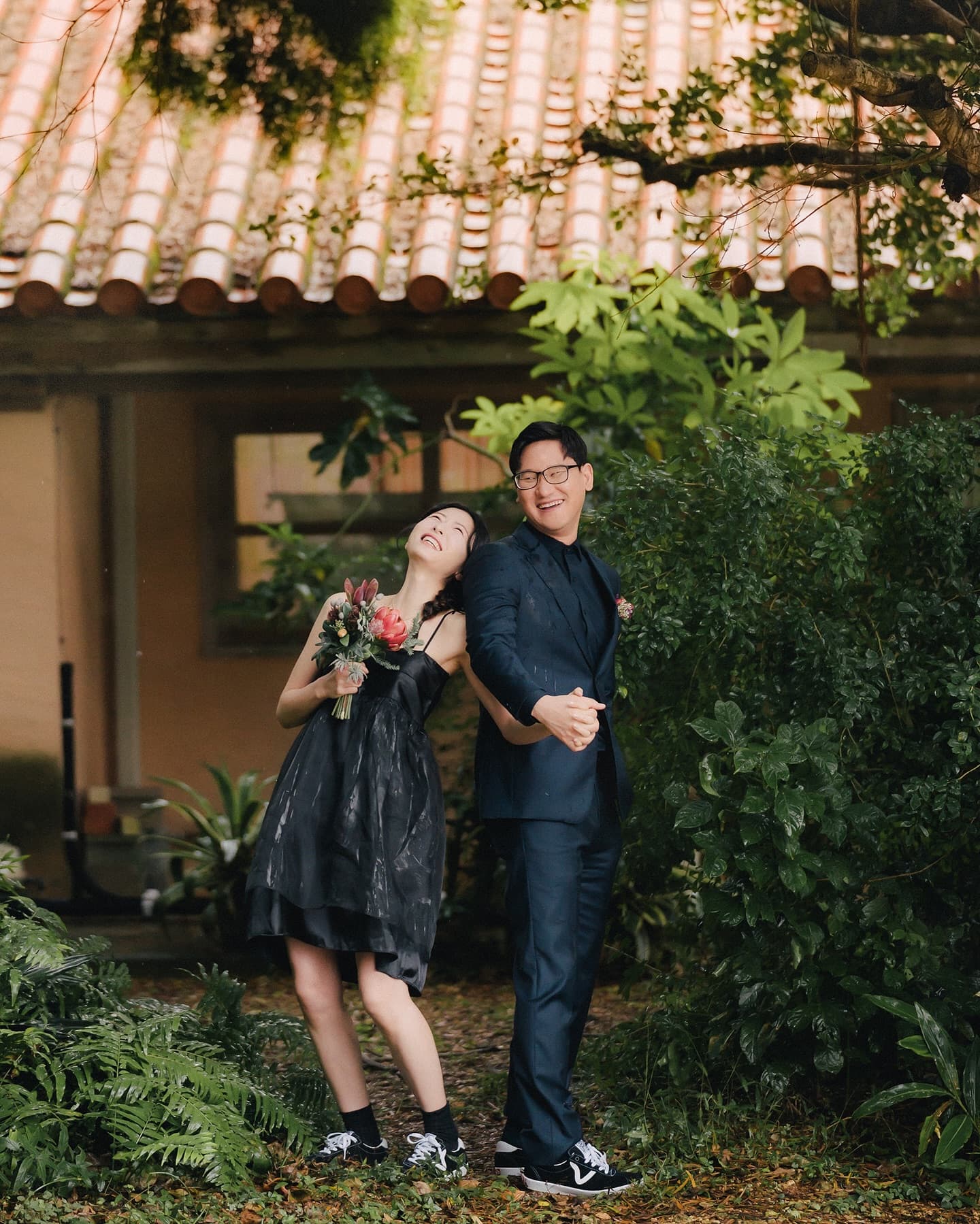 Couple laughing before a red-tiled Okinawan house on a rainy day