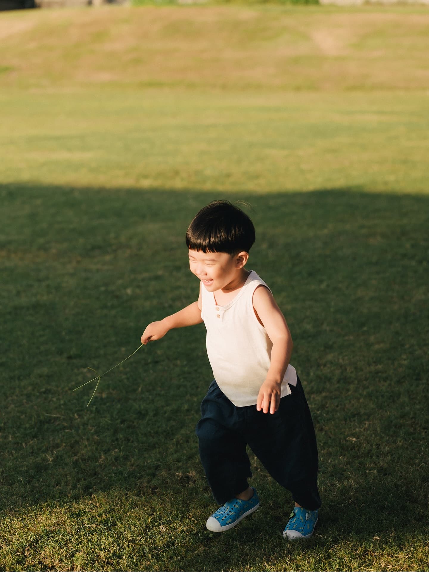 Little boy running across a sunlit grass field in Okinawa