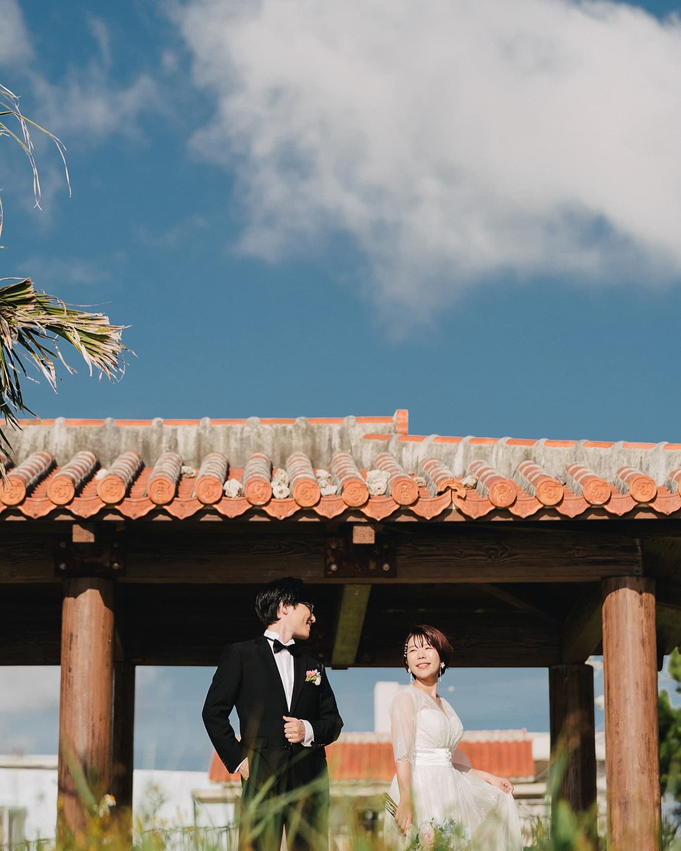 Couple beneath a red-tiled Okinawan pavilion under a wide blue sky