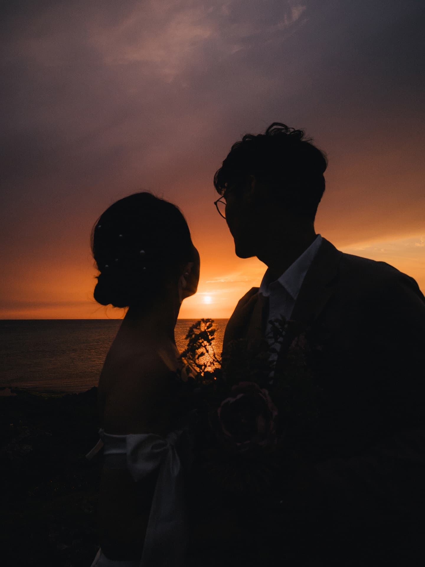 Couple silhouetted against an orange sunset over the Okinawa sea