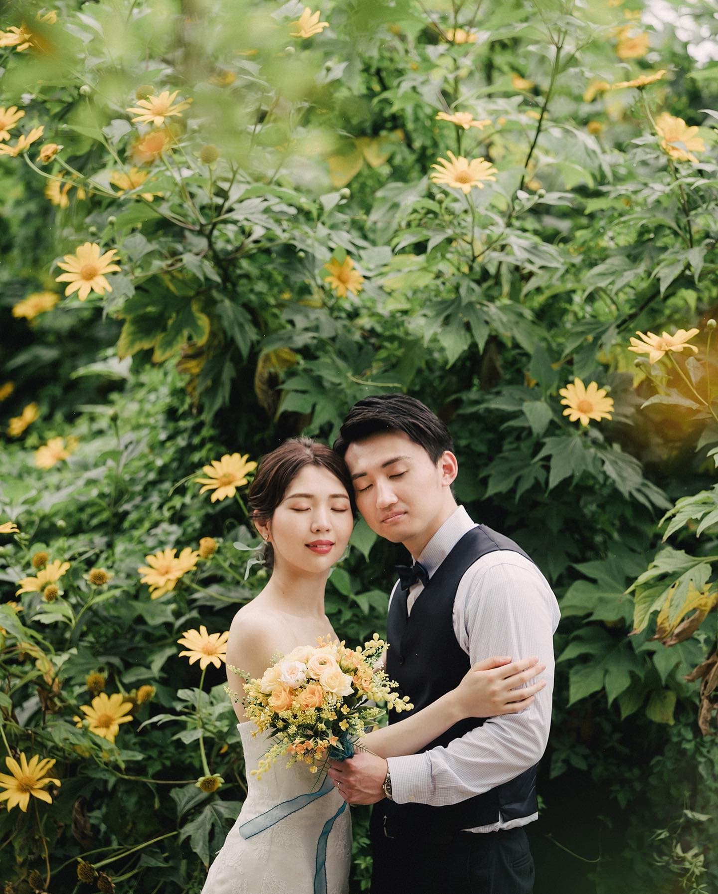 Couple resting cheek to cheek with eyes closed among yellow blooms, Okinawa