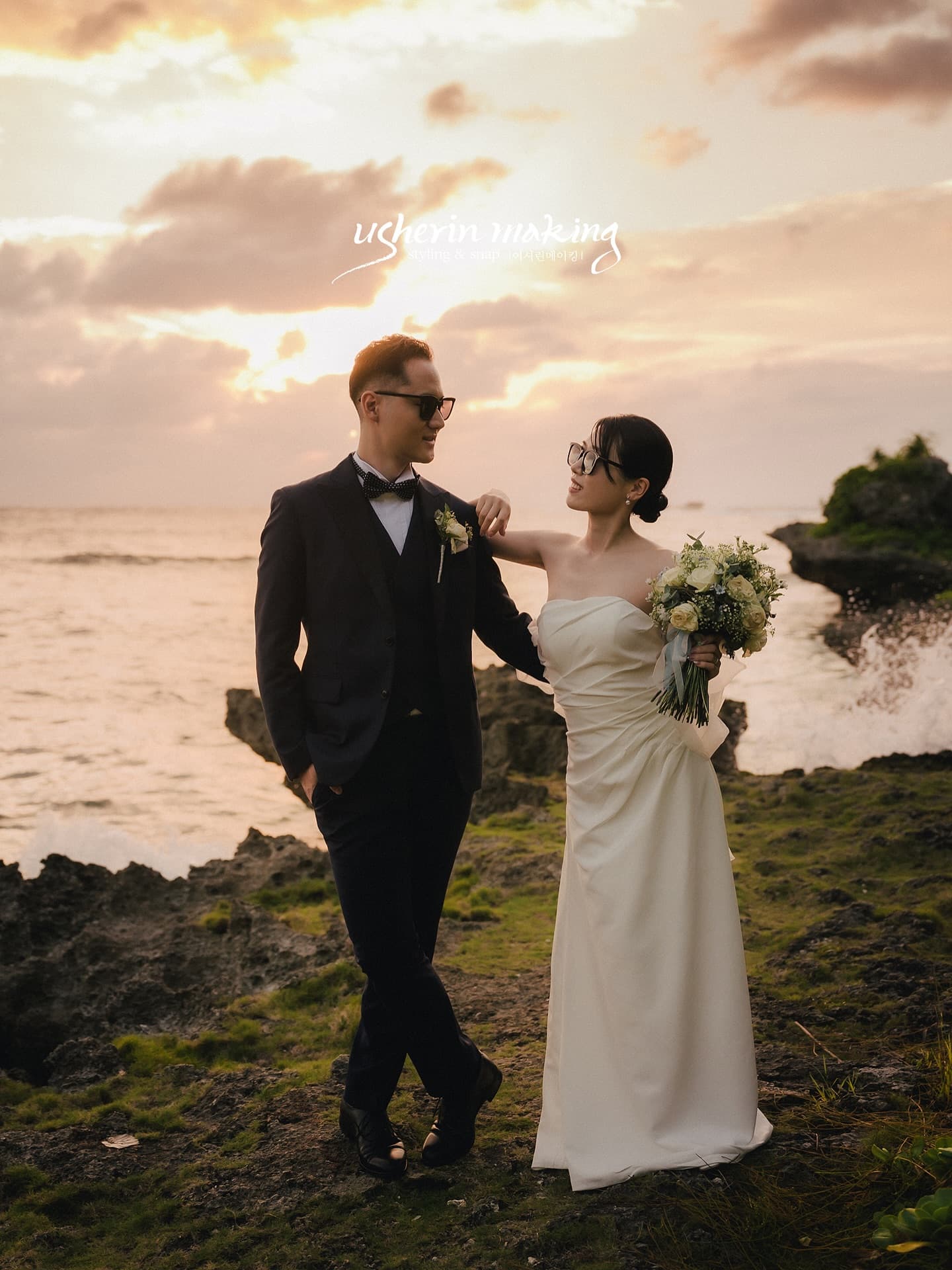 Bride and groom posing on a rocky shore under a glowing sunset sky in Okinawa