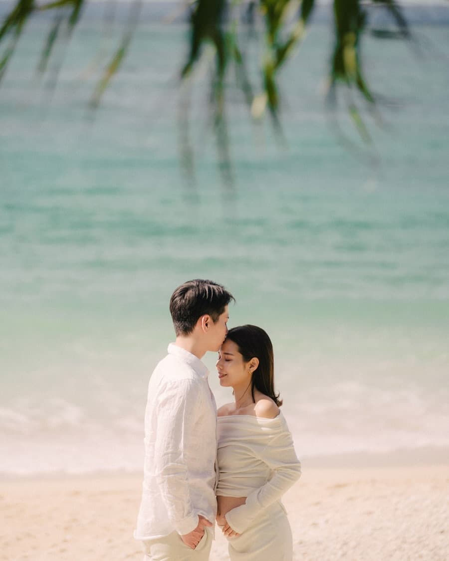 Husband kissing his wife's forehead on a beach by Okinawa's turquoise sea