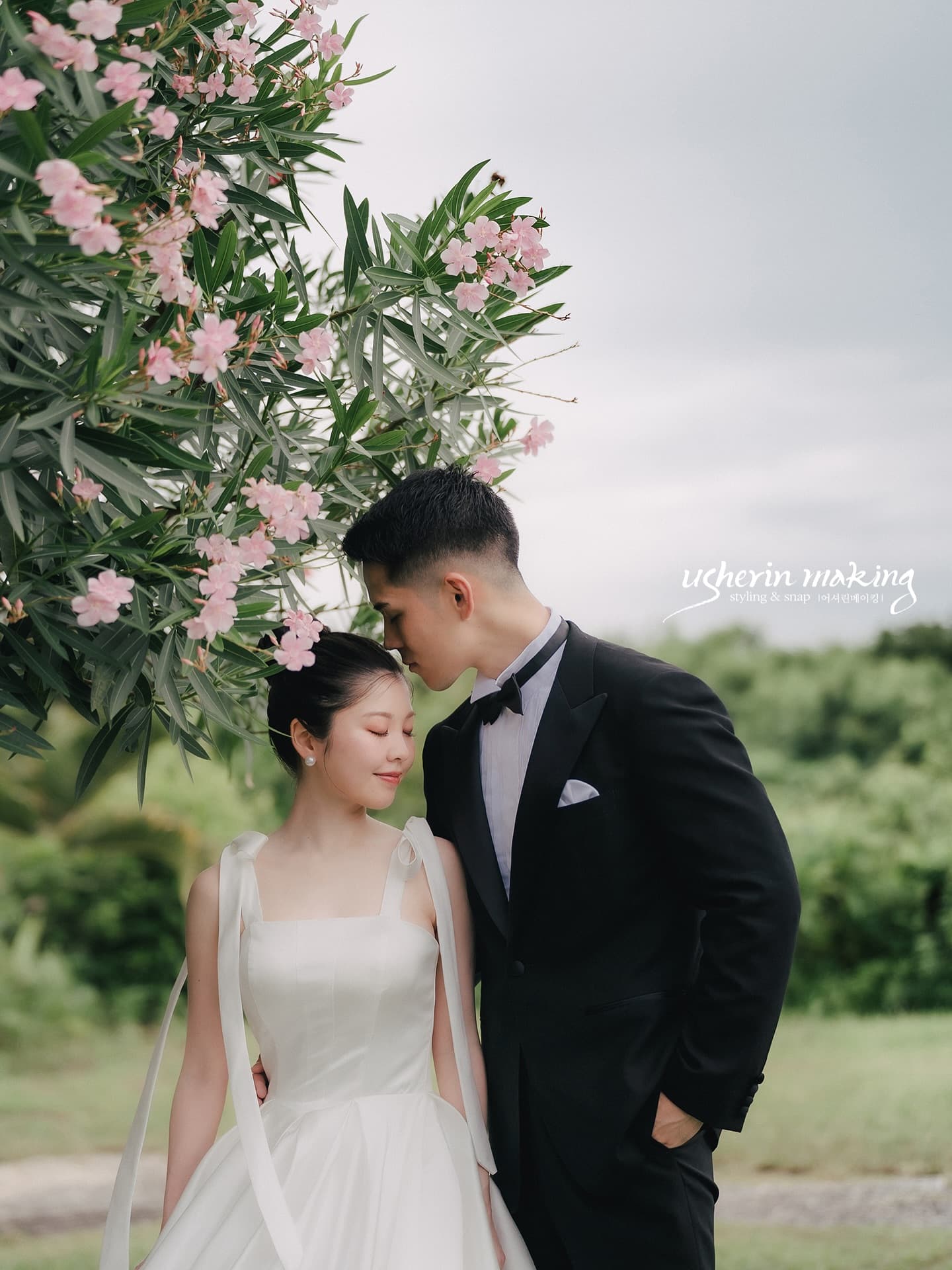 Groom kissing the bride's forehead under pink blossoms in Okinawa