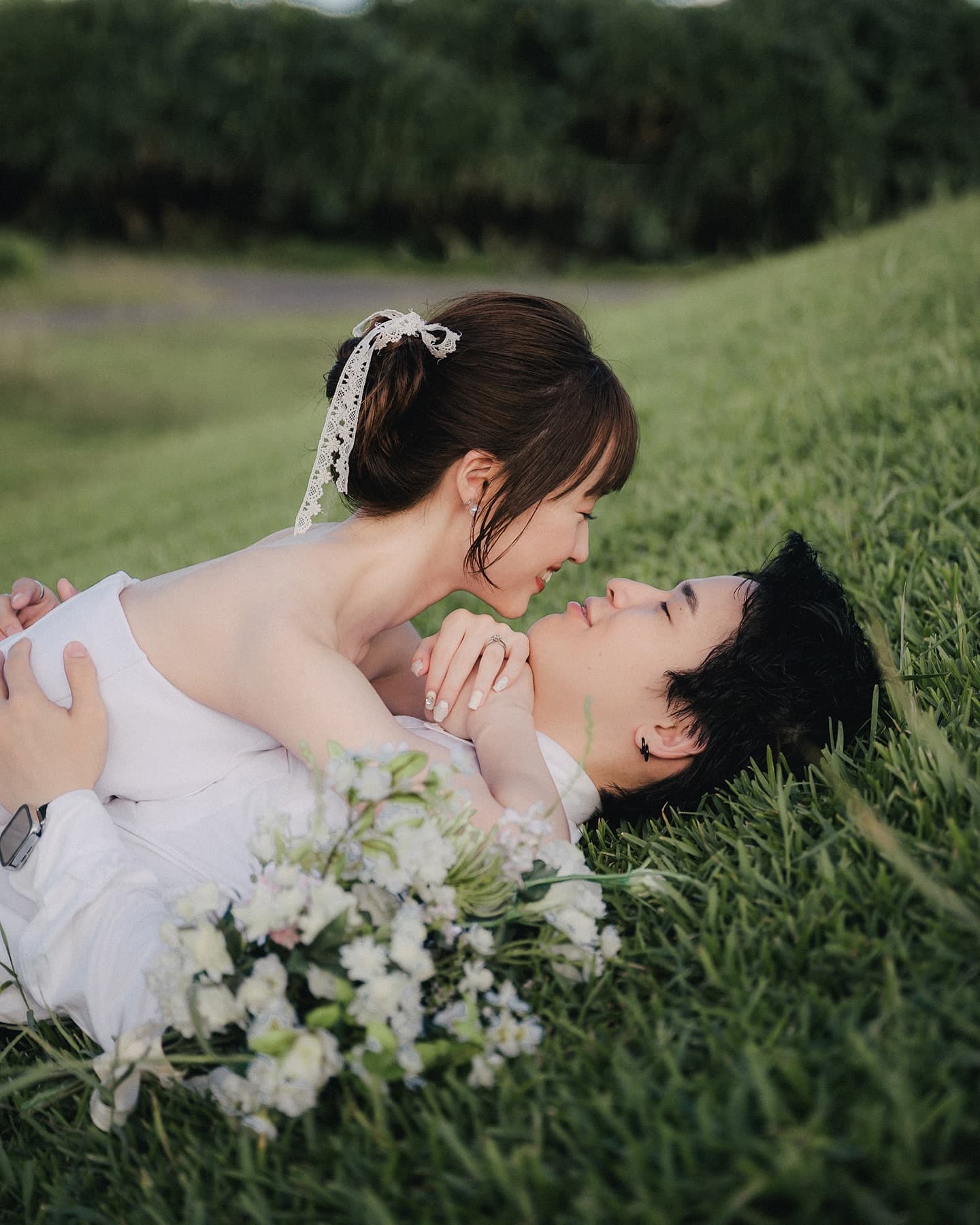 Couple lying on Okinawa grass, gazing at each other with a bouquet
