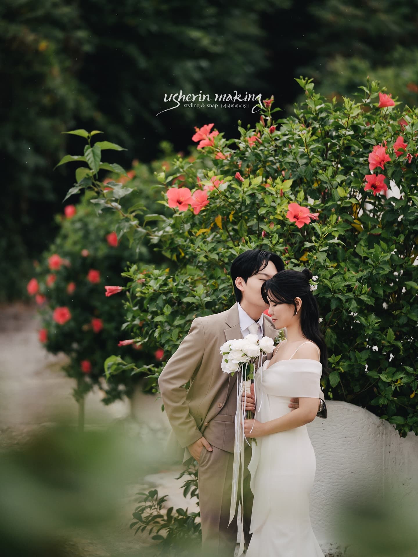 Groom kissing his bride's forehead among red hibiscus in Okinawa
